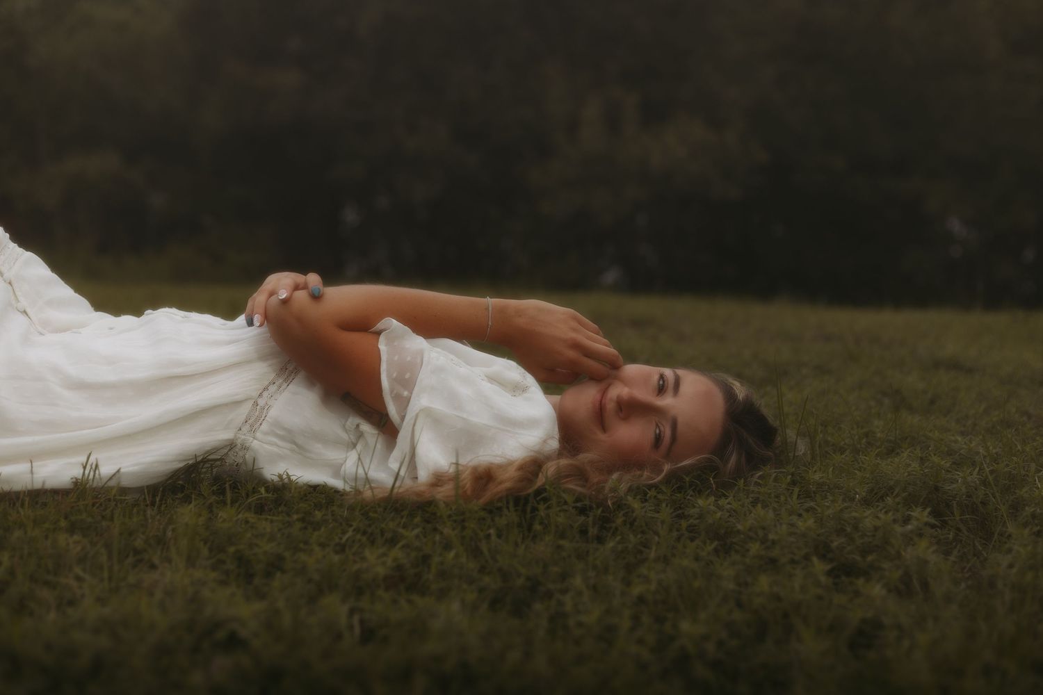 Person in white dress lying on grassy ground during golden hour sunset.