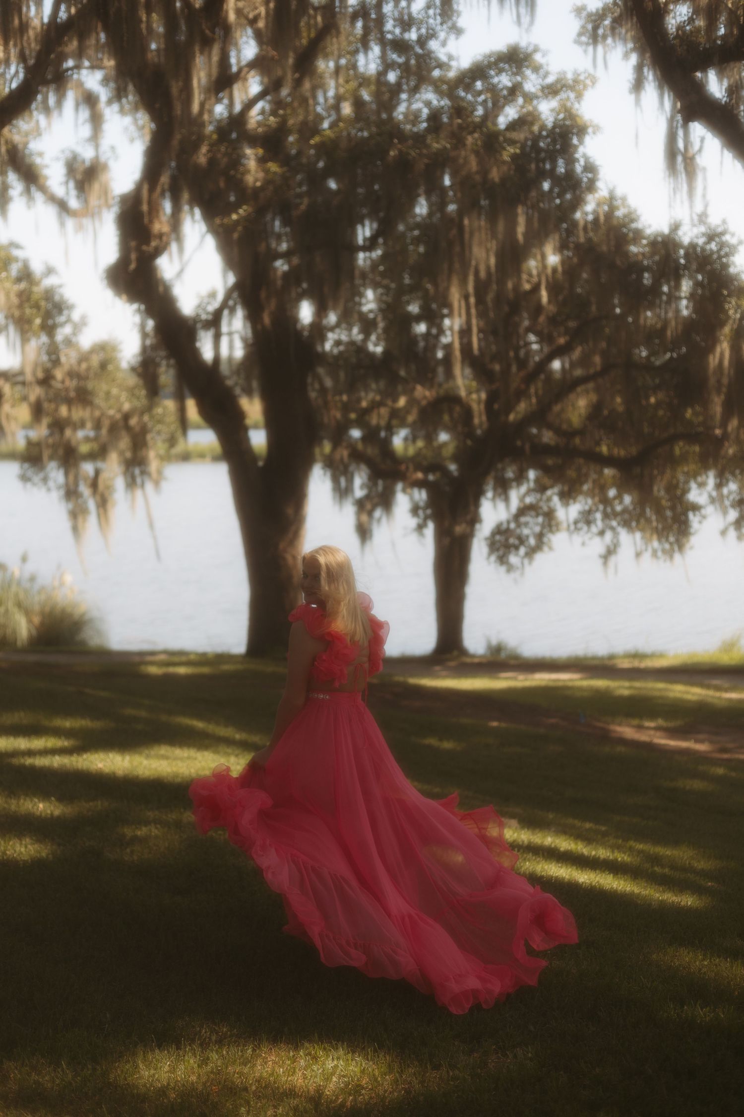 Flowing red dress catches sunlight beneath Spanish moss-draped trees in a romantic outdoor setting.