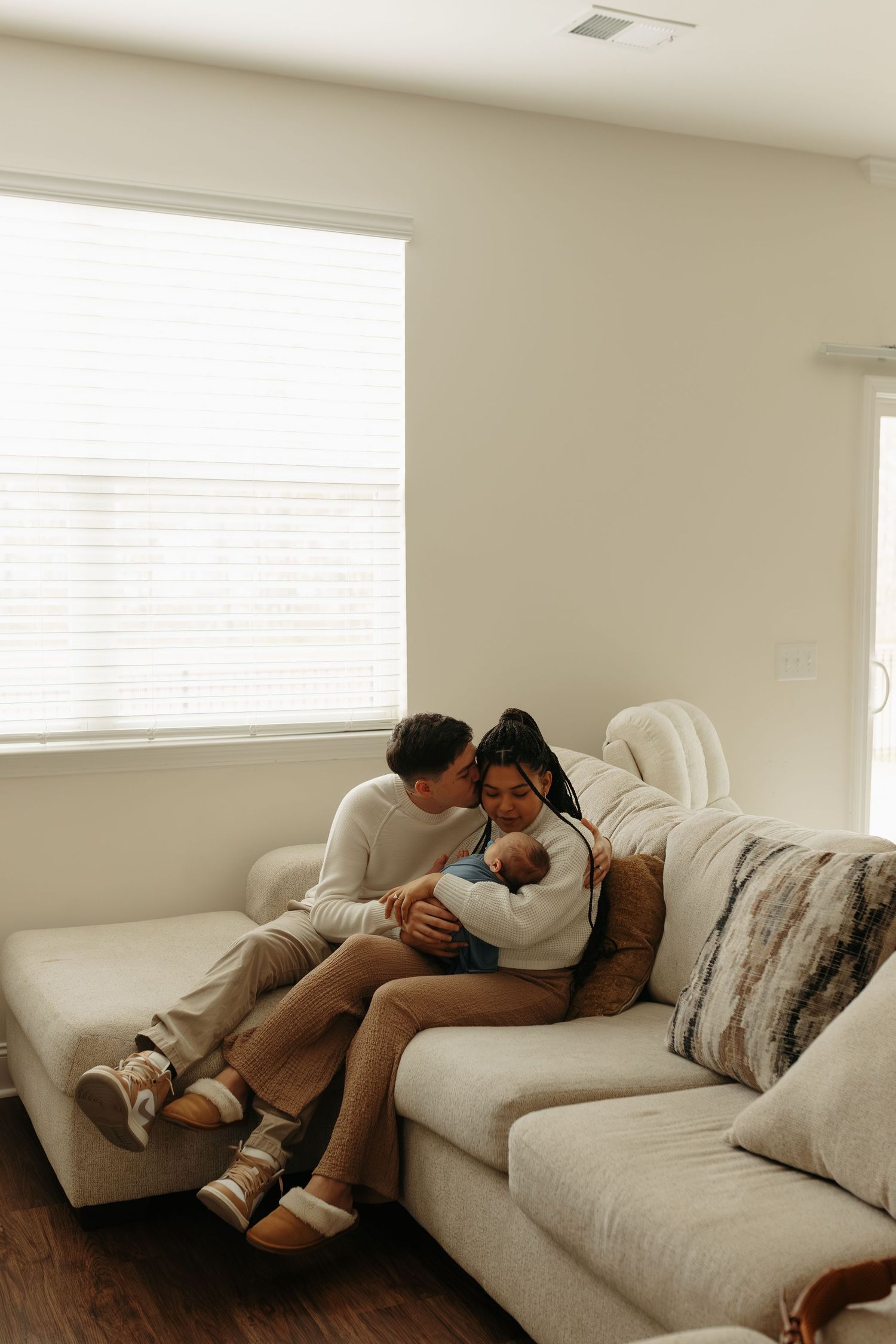 A couple rests together intimately on a white sectional sofa in a bright, minimalist living room.