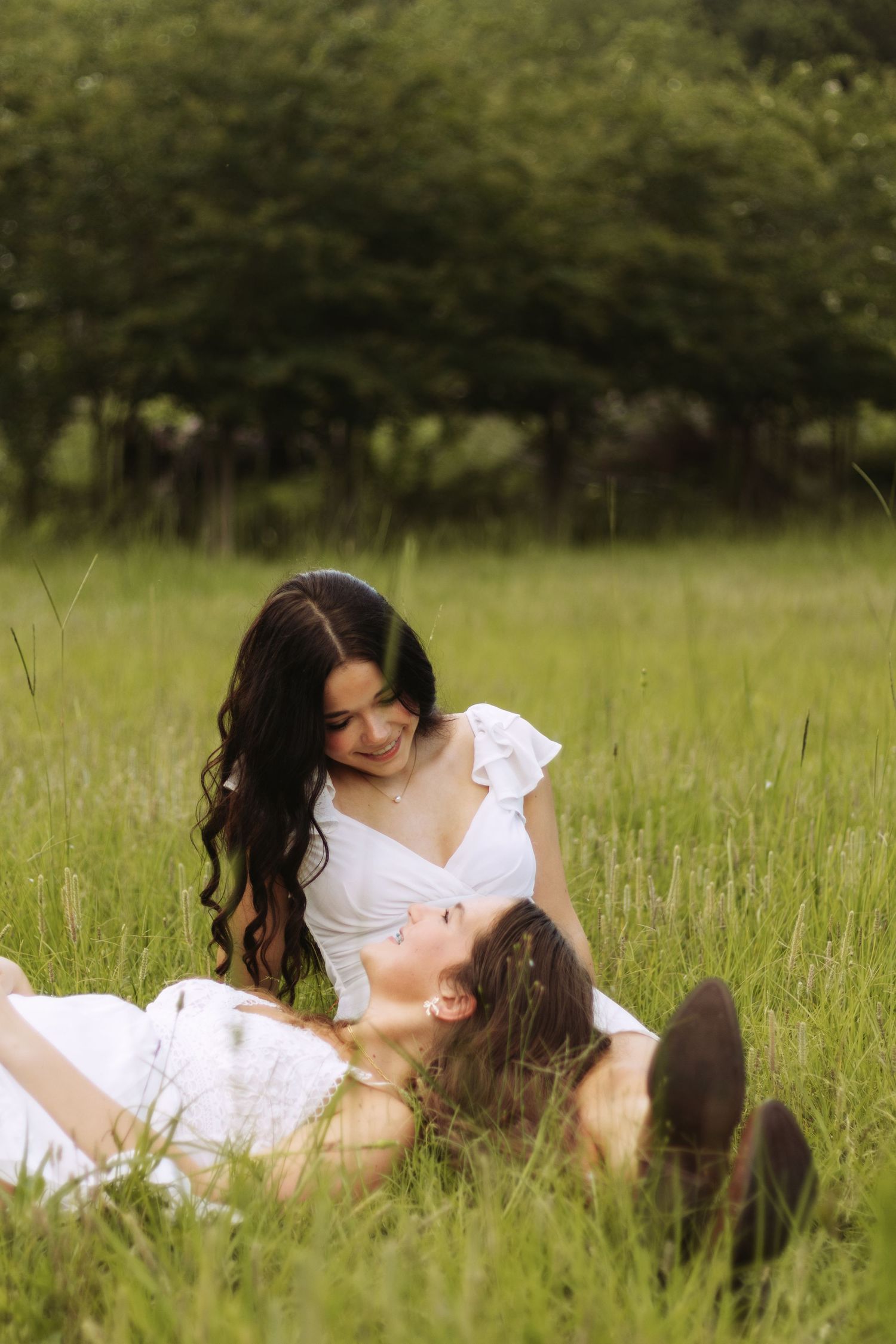 A tender moment shared between two people wearing white dresses as they relax in a sun-lit meadow of tall grass.
