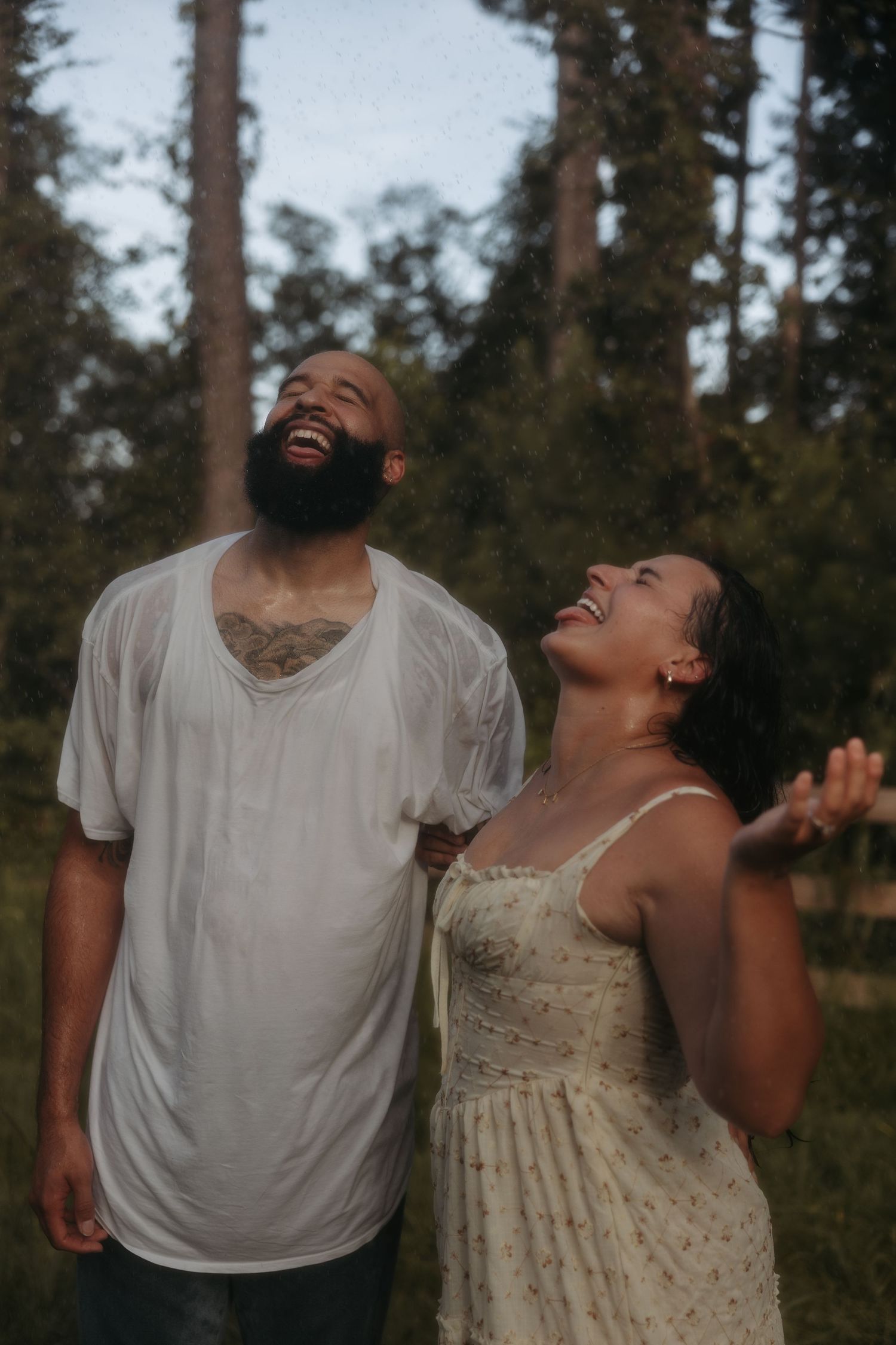 A couple shares an intimate candid moment of joy and laughter together in a forested outdoor setting.