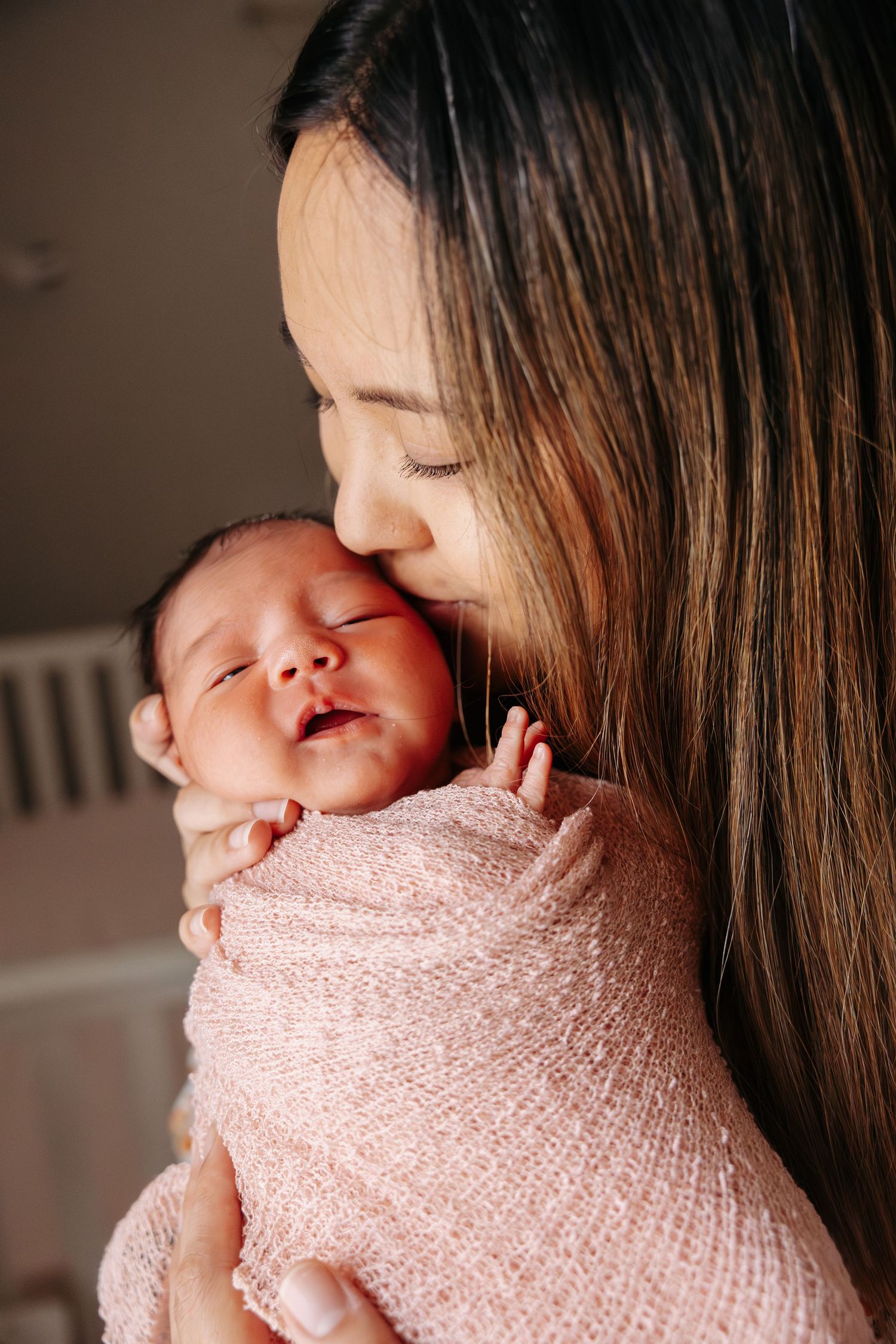 A tender moment as a mother cuddles her newborn baby wrapped in a soft pink knit blanket.