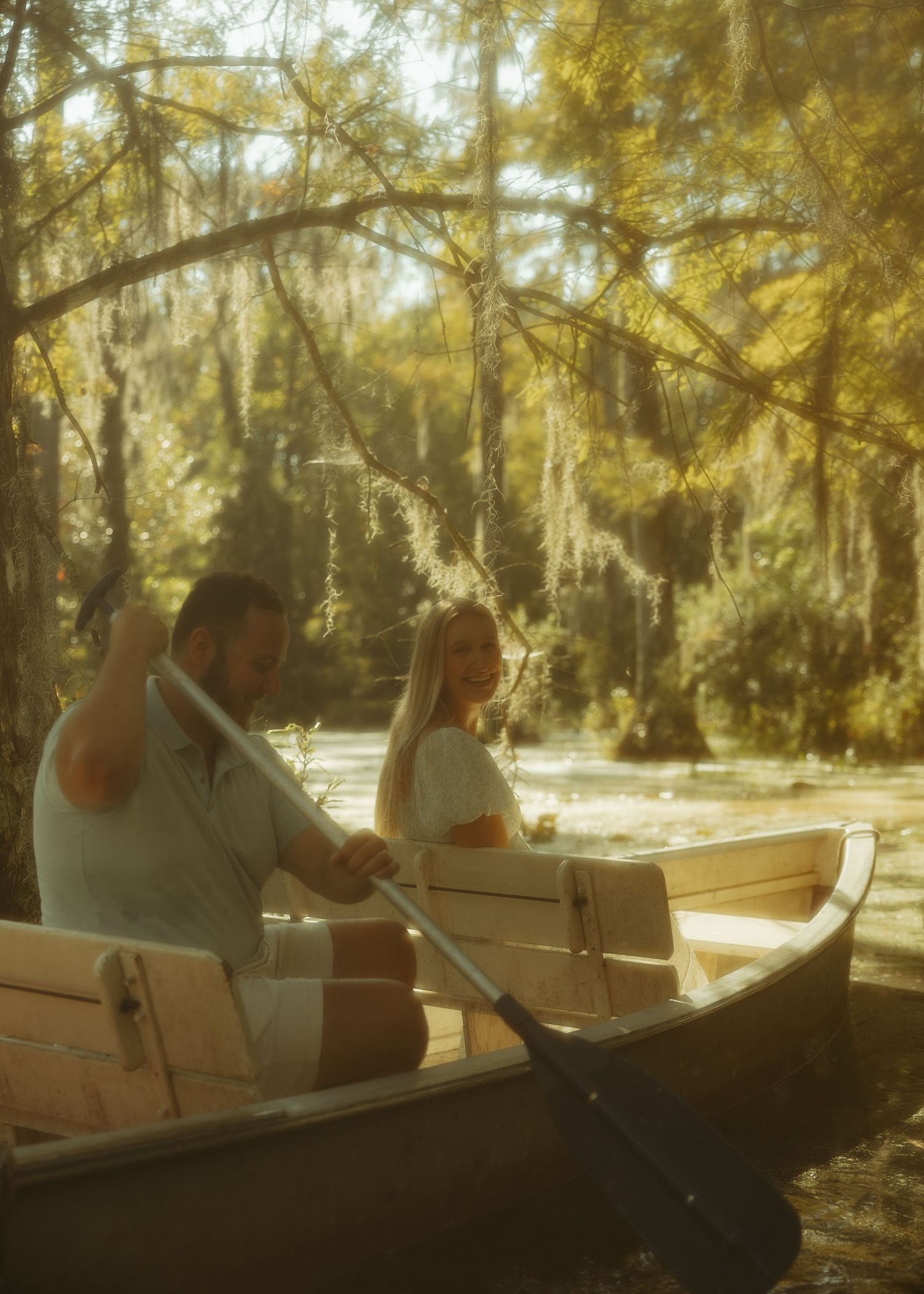 Couple canoeing through a sunlit cypress swamp with Spanish moss hanging from trees.