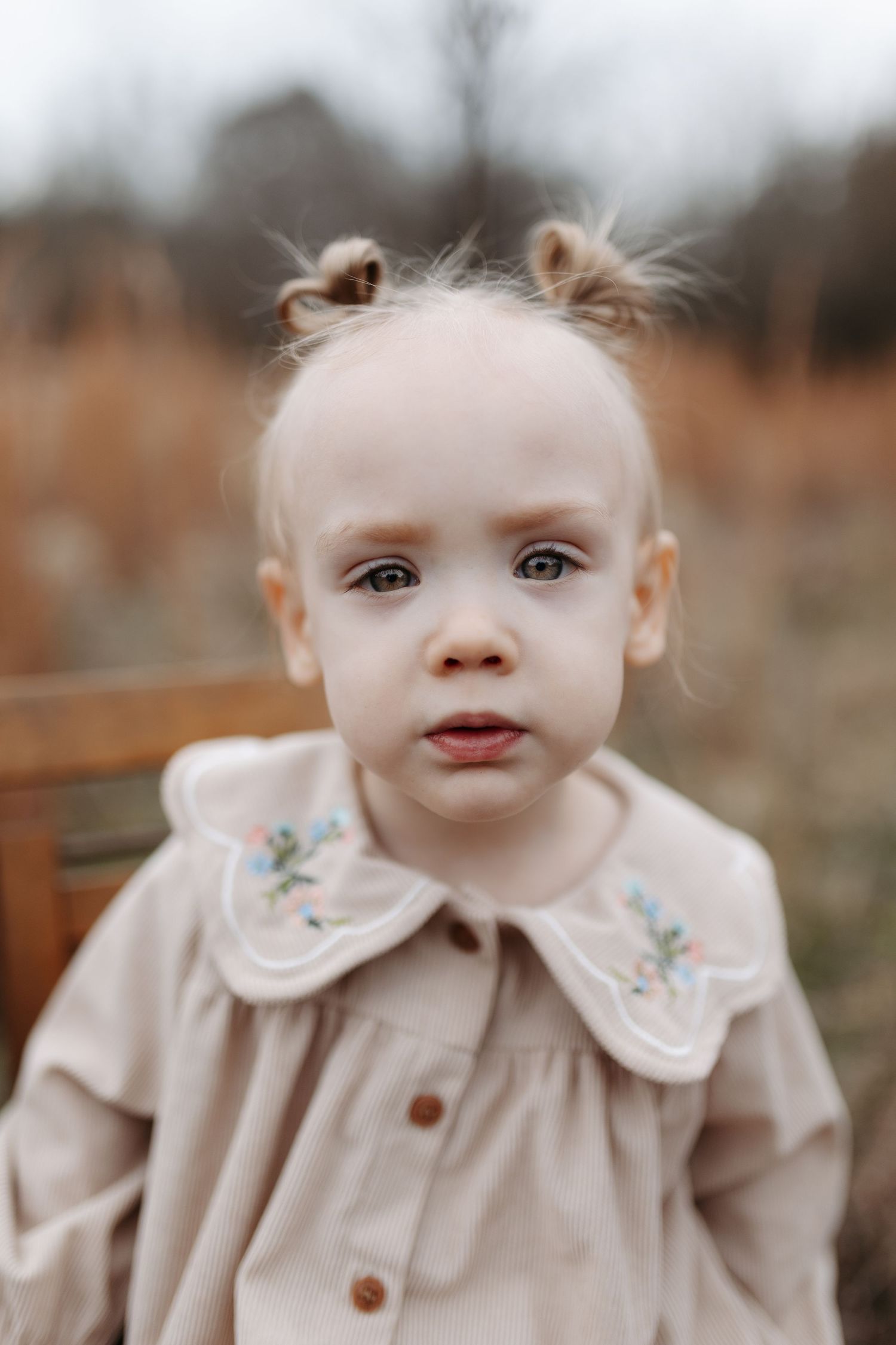 Baby in beige ruffled collar coat smiles sweetly in a series of outdoor autumn portraits.