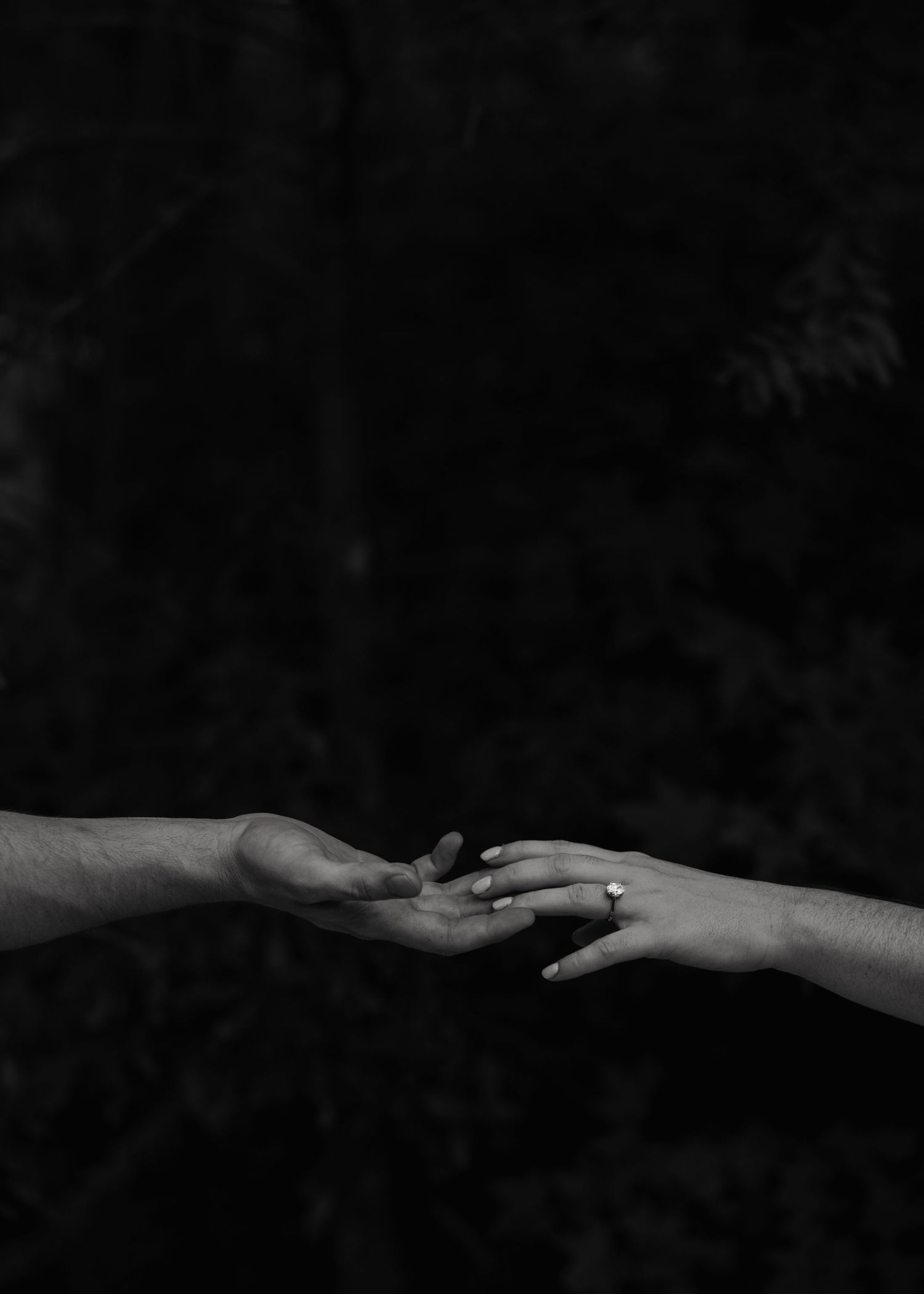 Black and white photo of two hands reaching toward each other against a dark background.