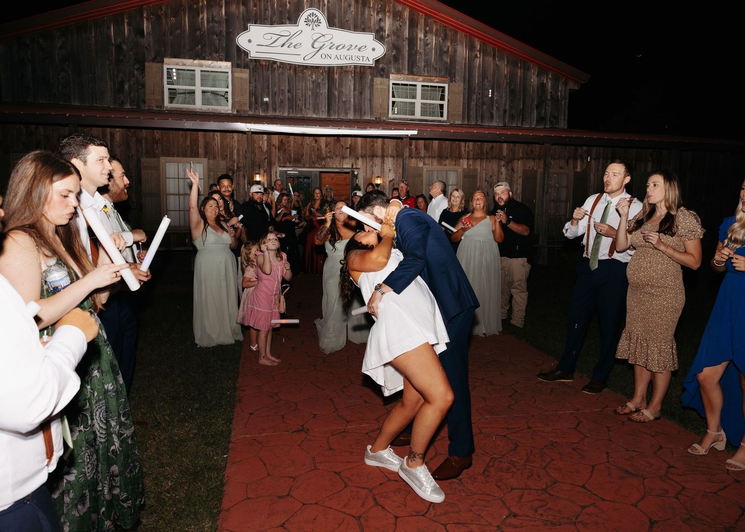 Bride and groom share romantic dip kiss during outdoor wedding reception sendoff at night.
