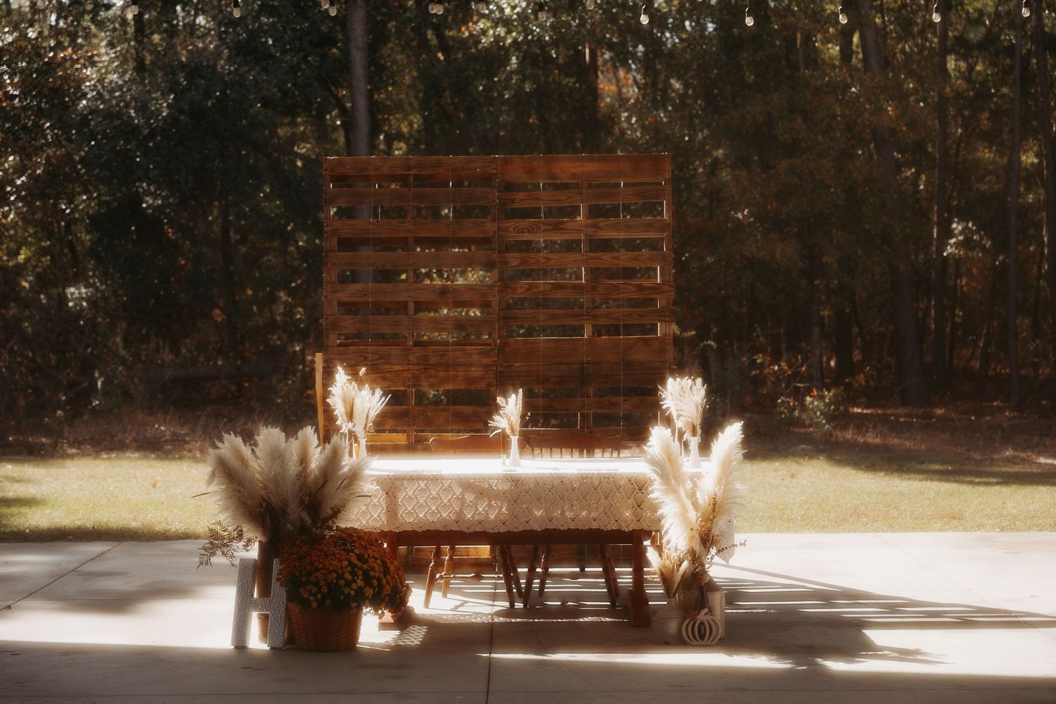 Rustic wooden pallet backdrop with pampas grass and floral arrangements on a sunlit outdoor patio.