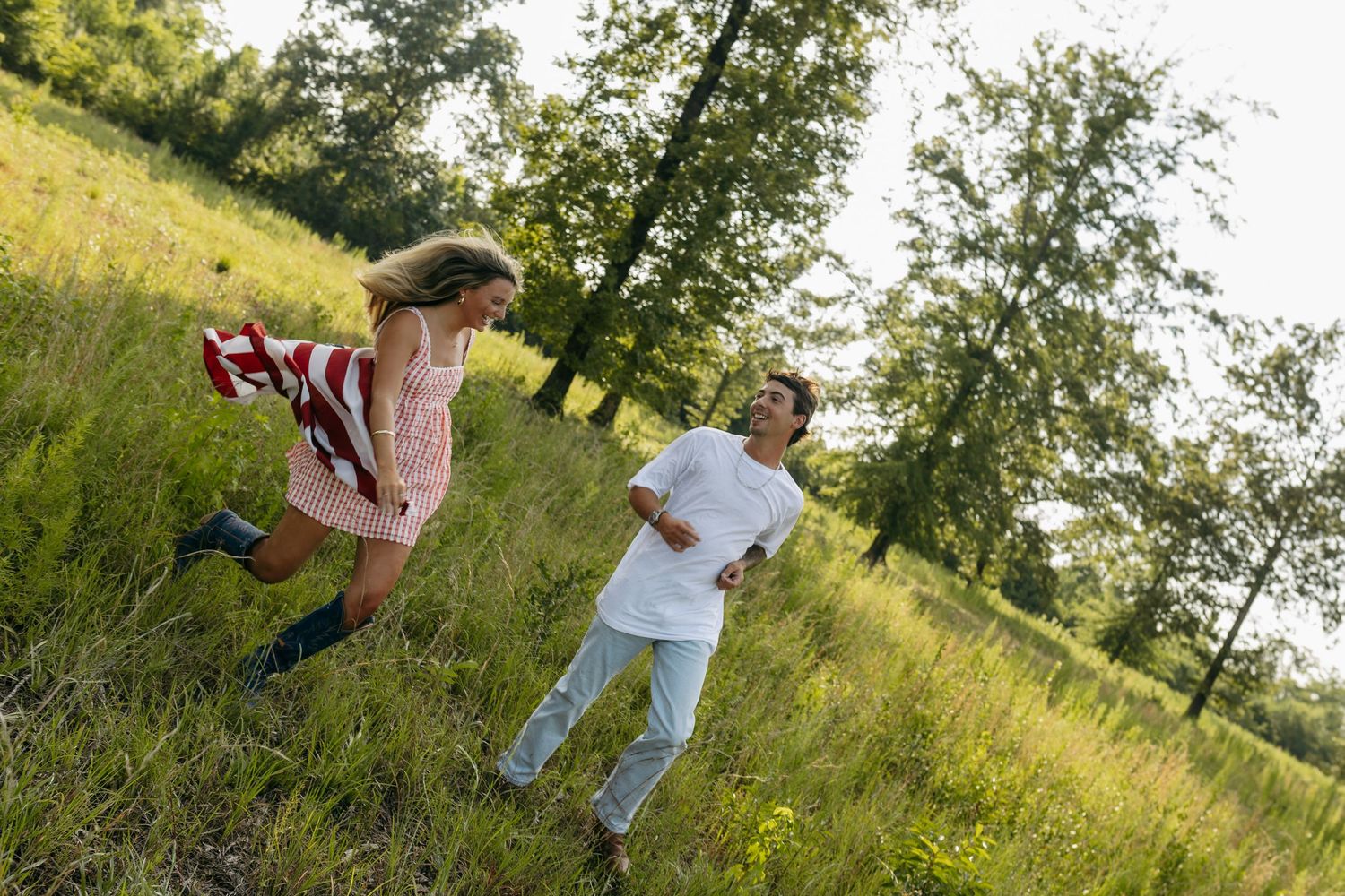 Young couple running and playing together in a lush green meadow surrounded by trees on a sunny day.