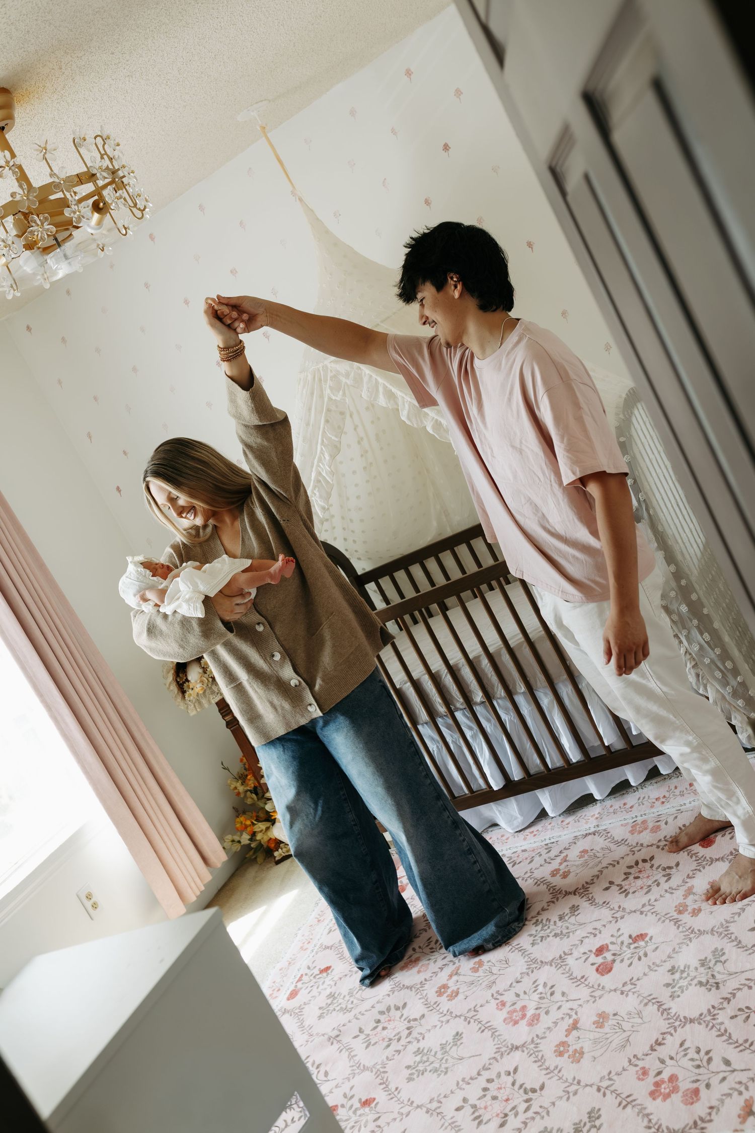 A young couple dancing together in a pastel nursery room with a vintage crib and floral rug.