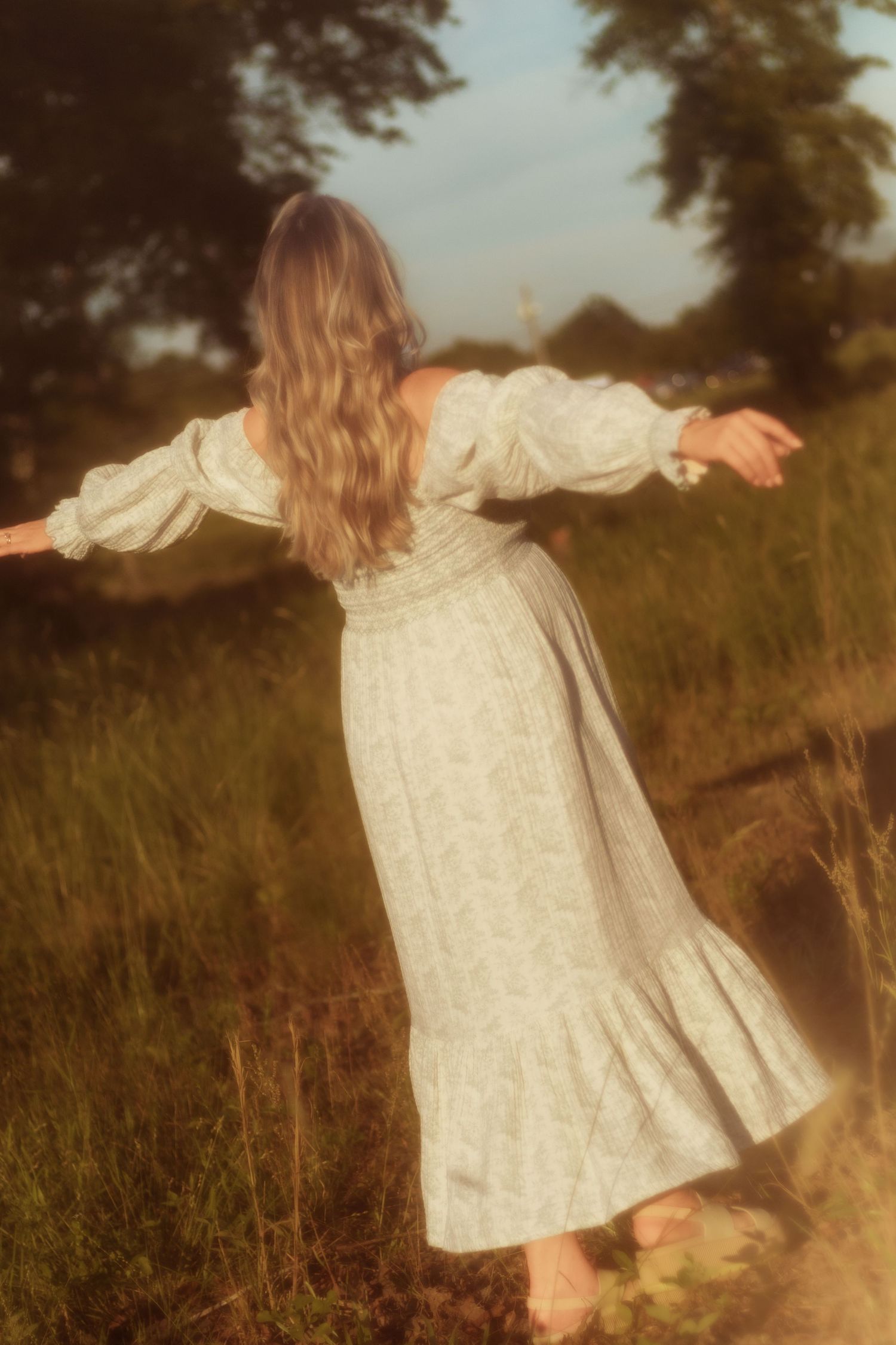 Figure in flowing white dress spins joyfully in a sun-drenched field.