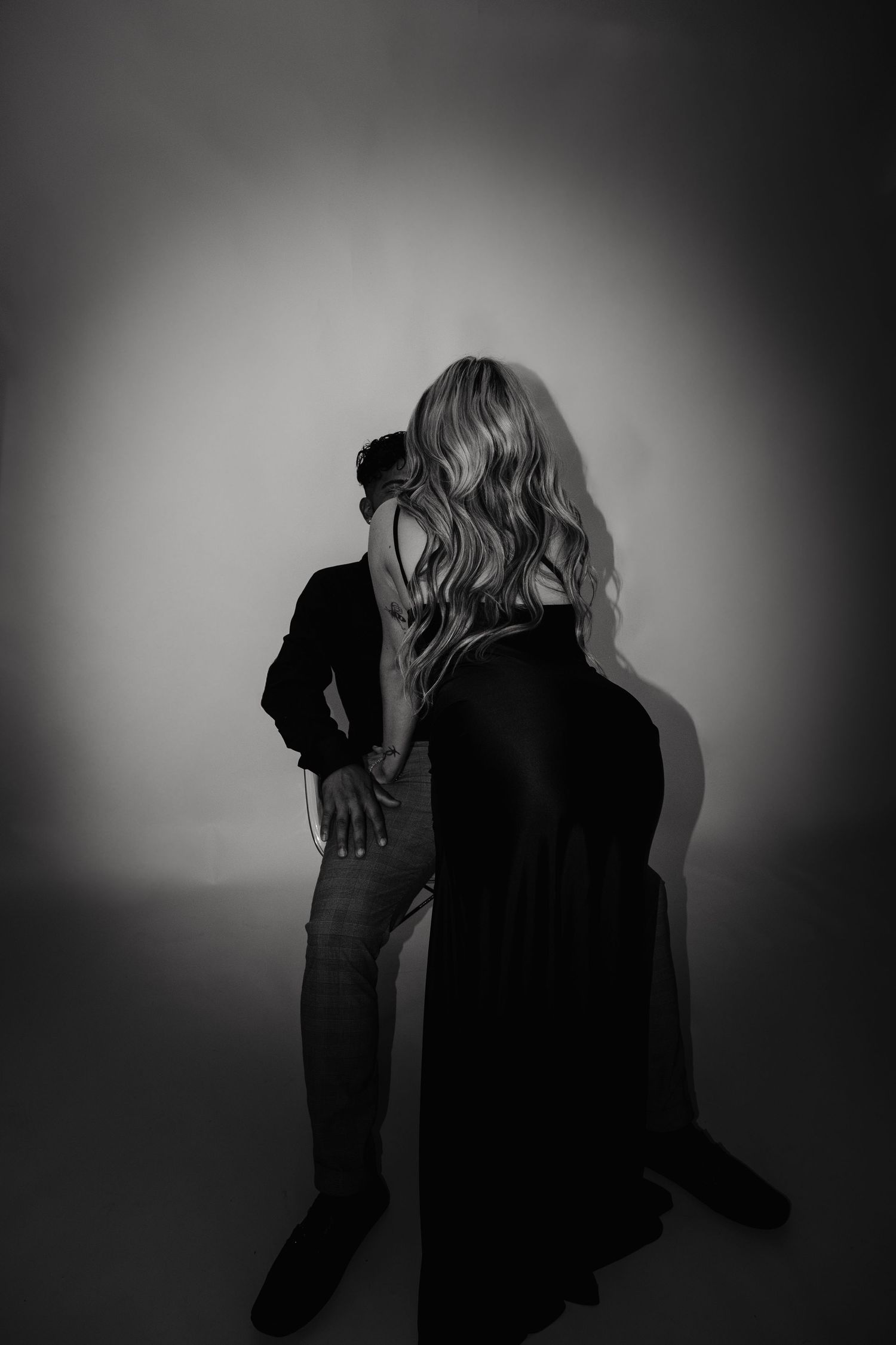 Black and white photo of a couple embracing, woman in flowing black gown with long wavy hair, man in dark jacket.