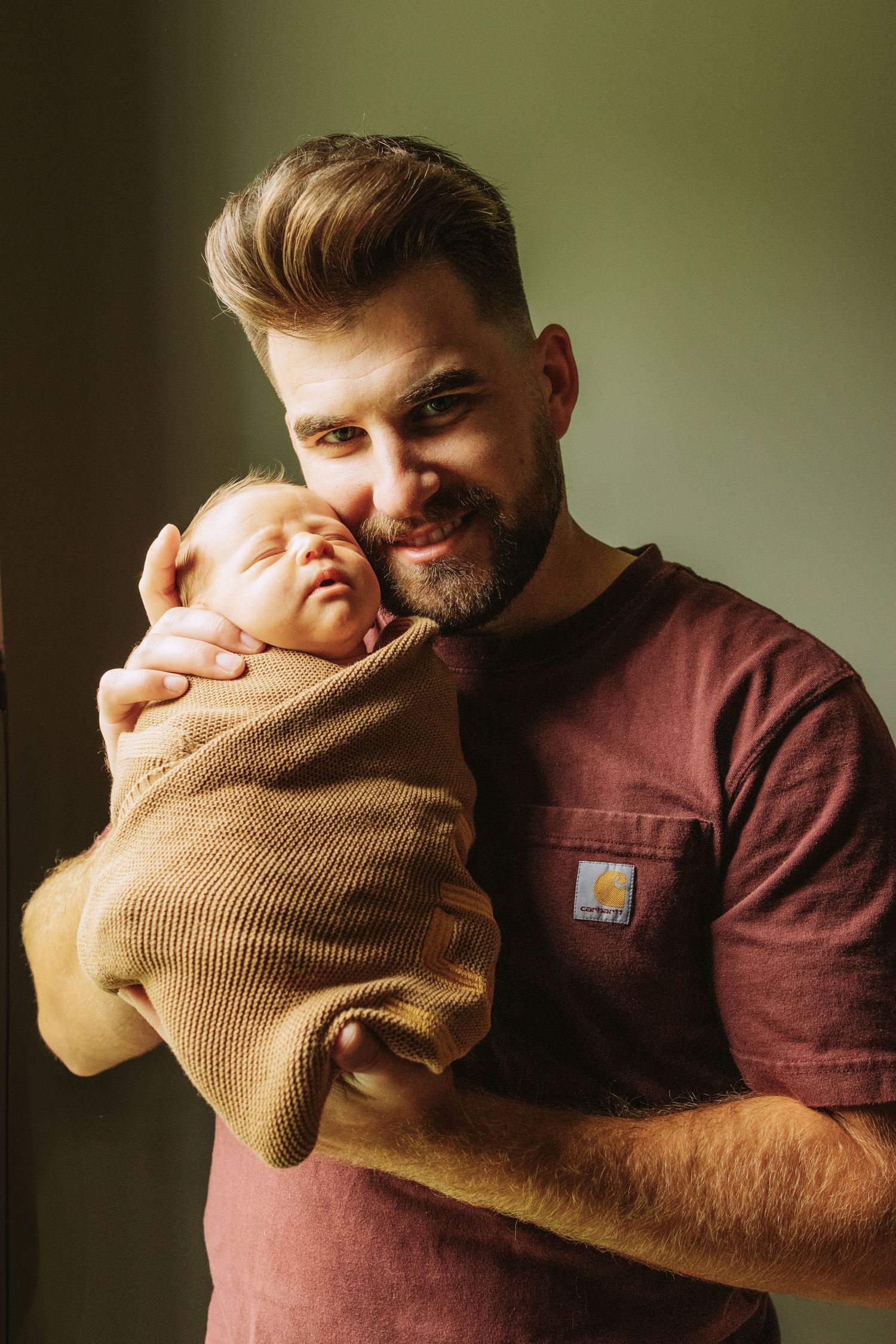 Tender moment captured as someone holds a newborn baby wrapped in a brown knit blanket against their chest.
