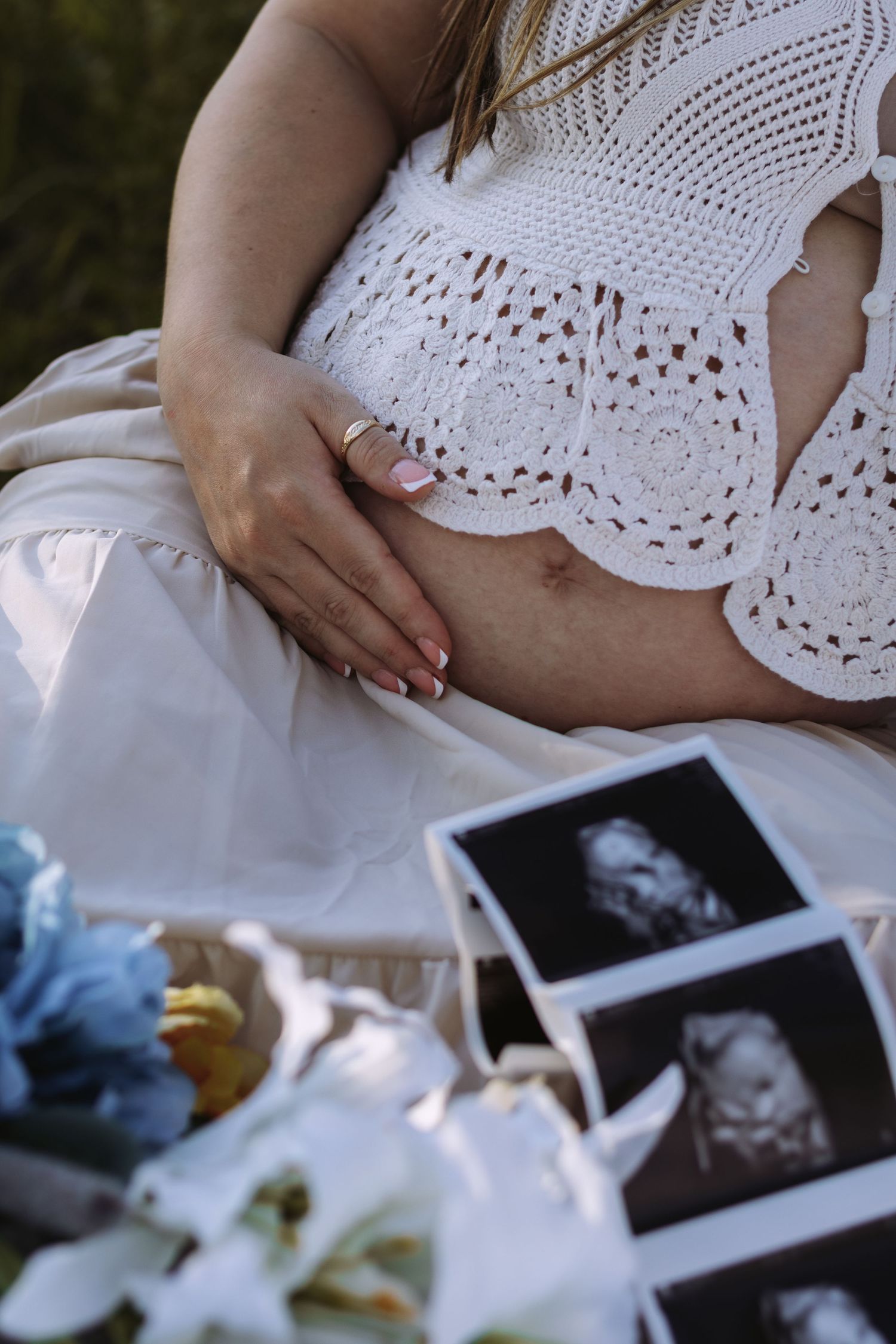 Maternity photo showing pregnant belly in white crochet top with ultrasound images and white lilies.