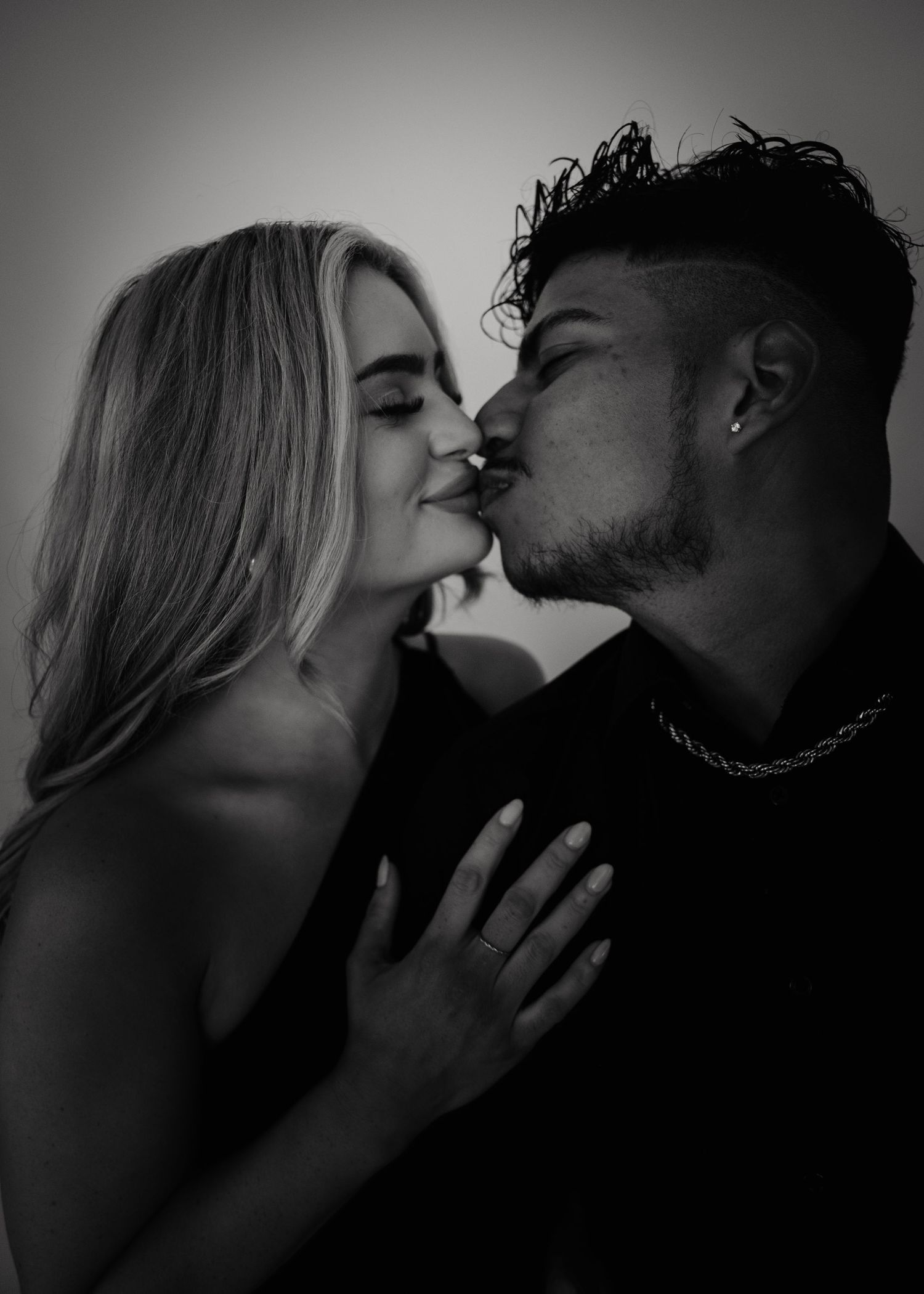 A romantic black and white portrait of a couple sharing an intimate kiss in dramatic lighting.