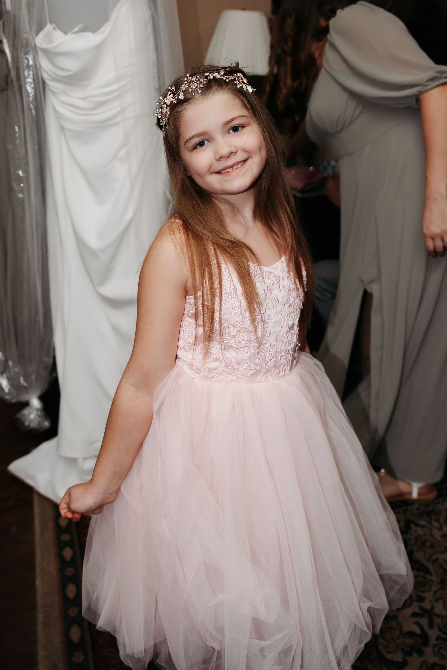 Young flower girl in pink tulle dress and floral crown smiles at wedding celebration.
