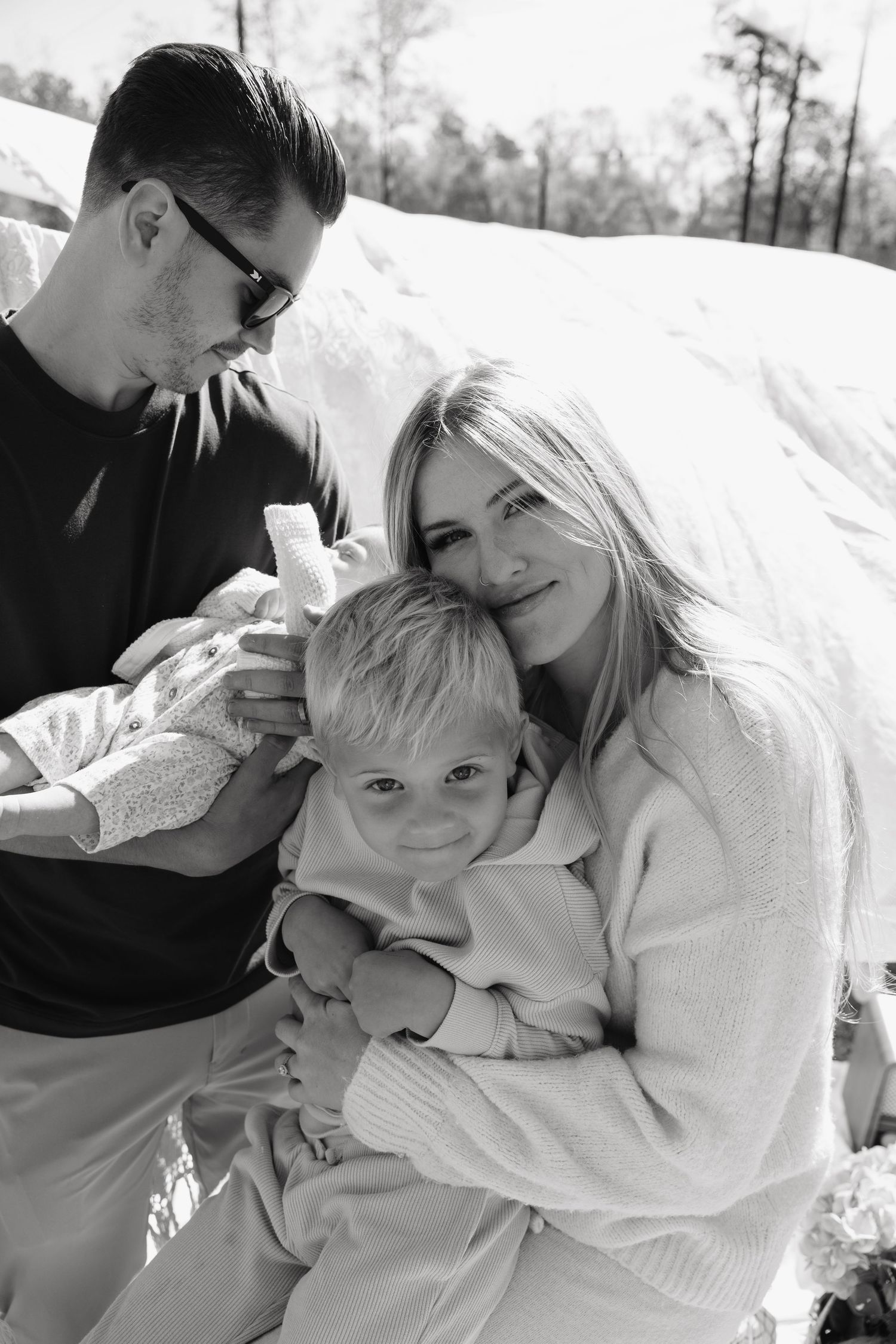 Black and white family portrait with parents and young child outdoors in snowy setting, warm and intimate moment.