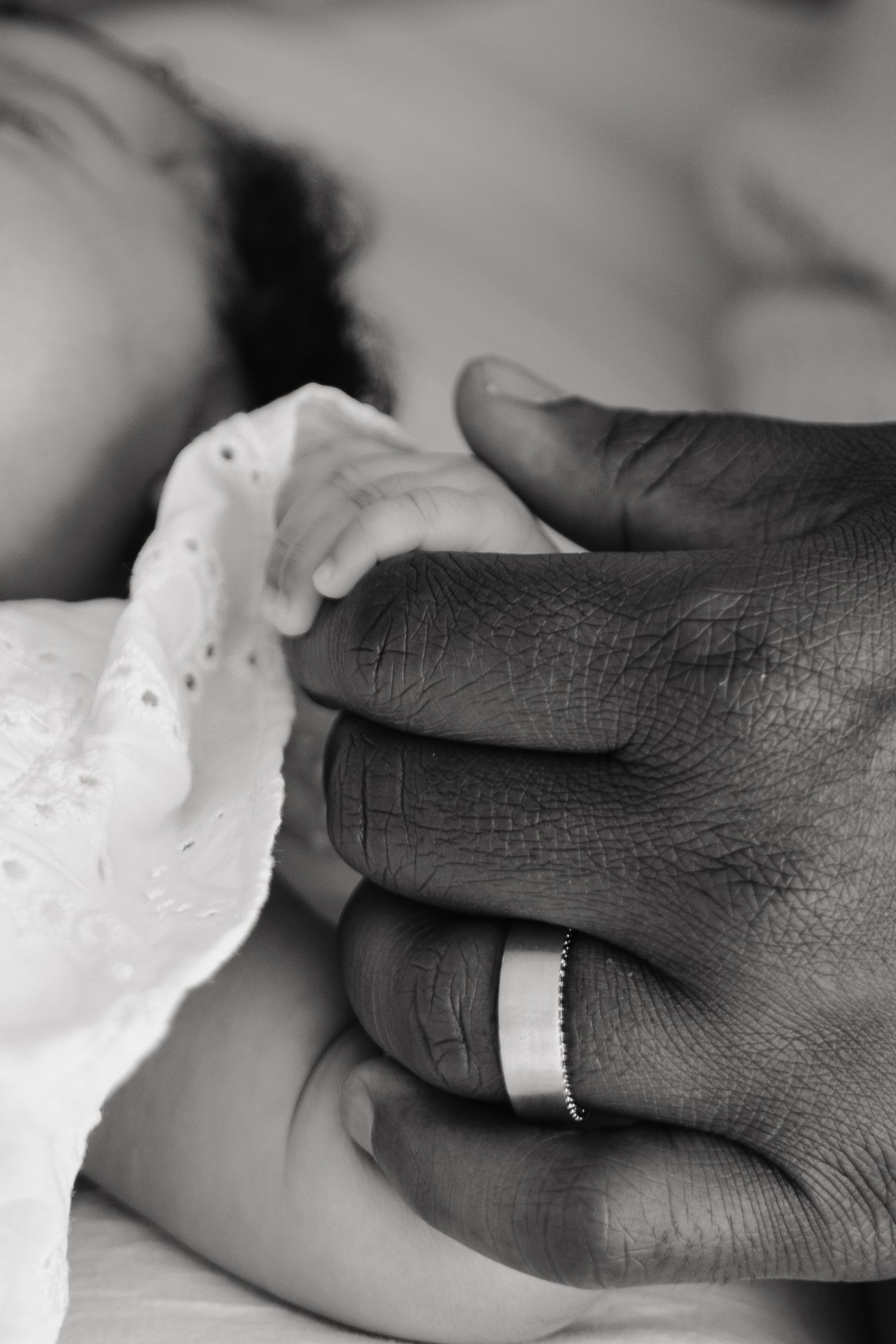 Black and white photo of a newborn baby's hand held by a parent wearing a wedding ring.