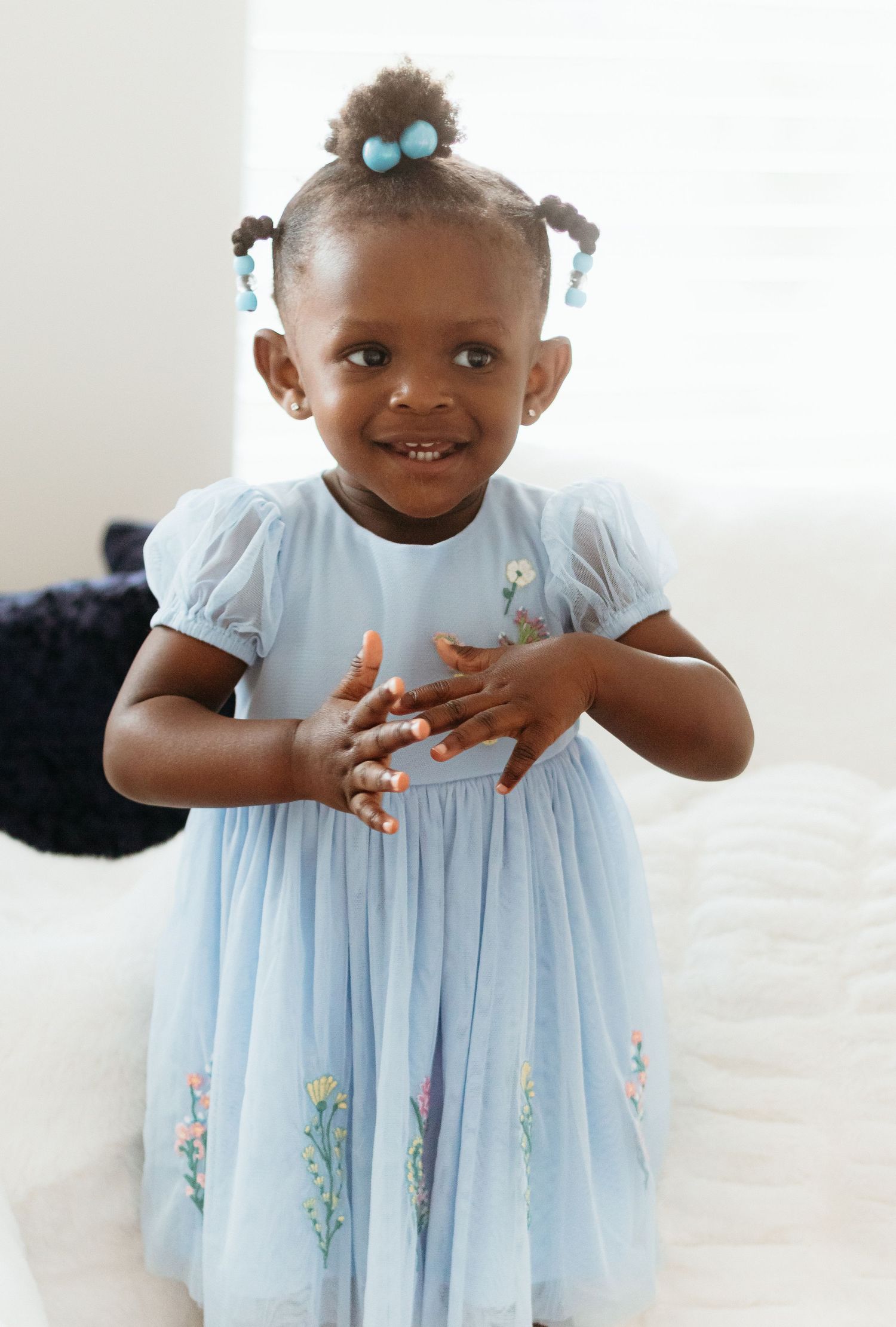 Small child in a light blue floral dress playing and posing indoors.