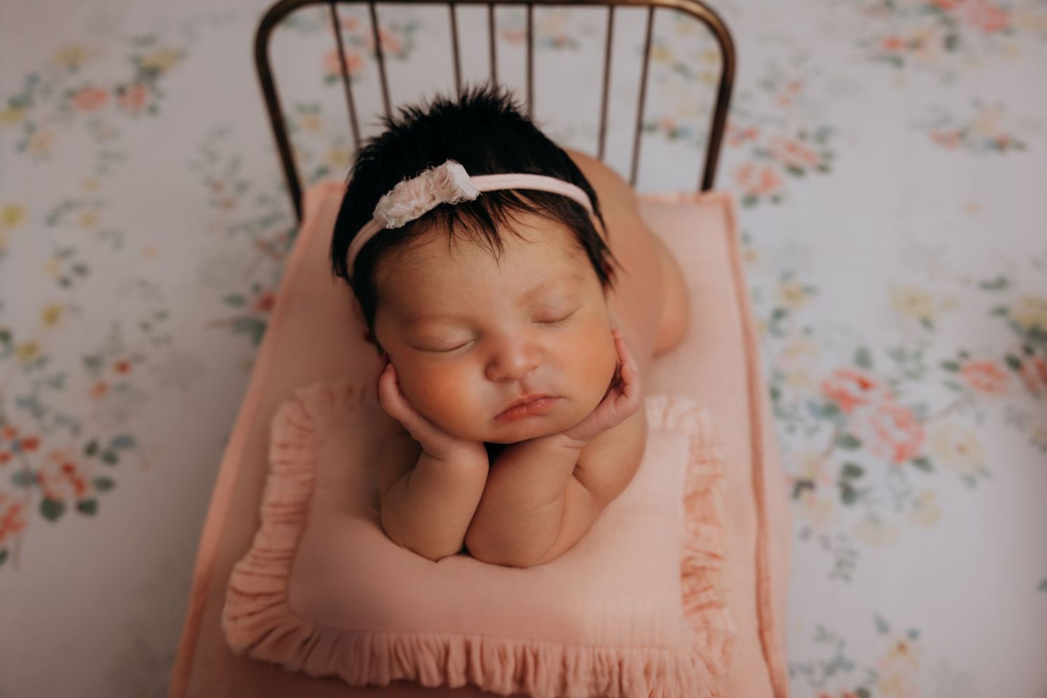 A sleeping newborn baby in a peach-colored wrap against a floral backdrop.