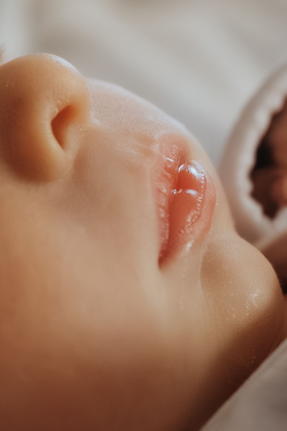 Close-up profile view of a baby's face with soft skin and pink lips in a serene sleeping pose.
