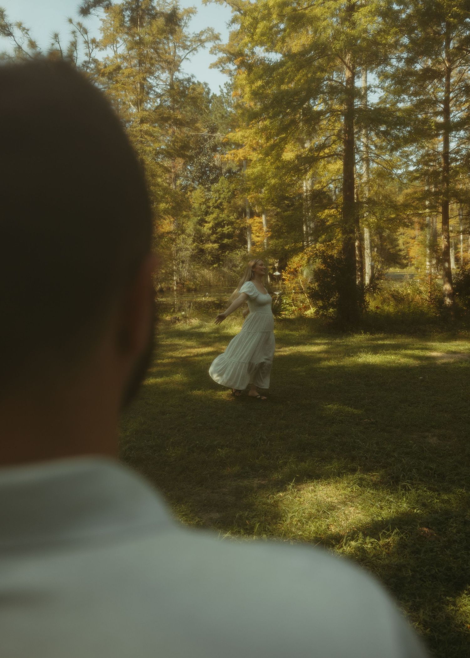 Sequence of shots showing a twirling figure in a white dress dancing among sunlit trees in a wooded area.