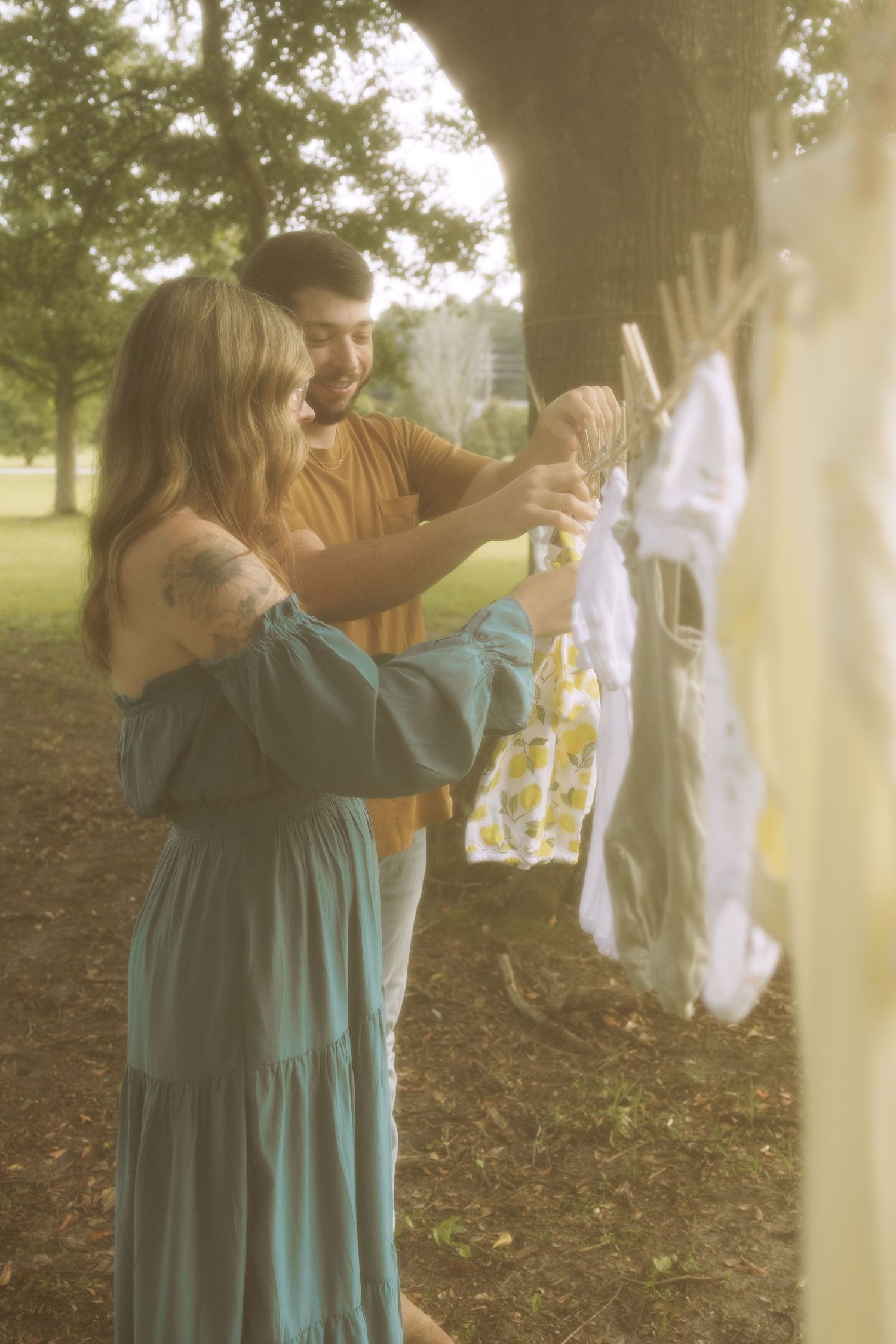 A person in a teal dress hangs white linens on a clothesline outdoors in misty morning light.