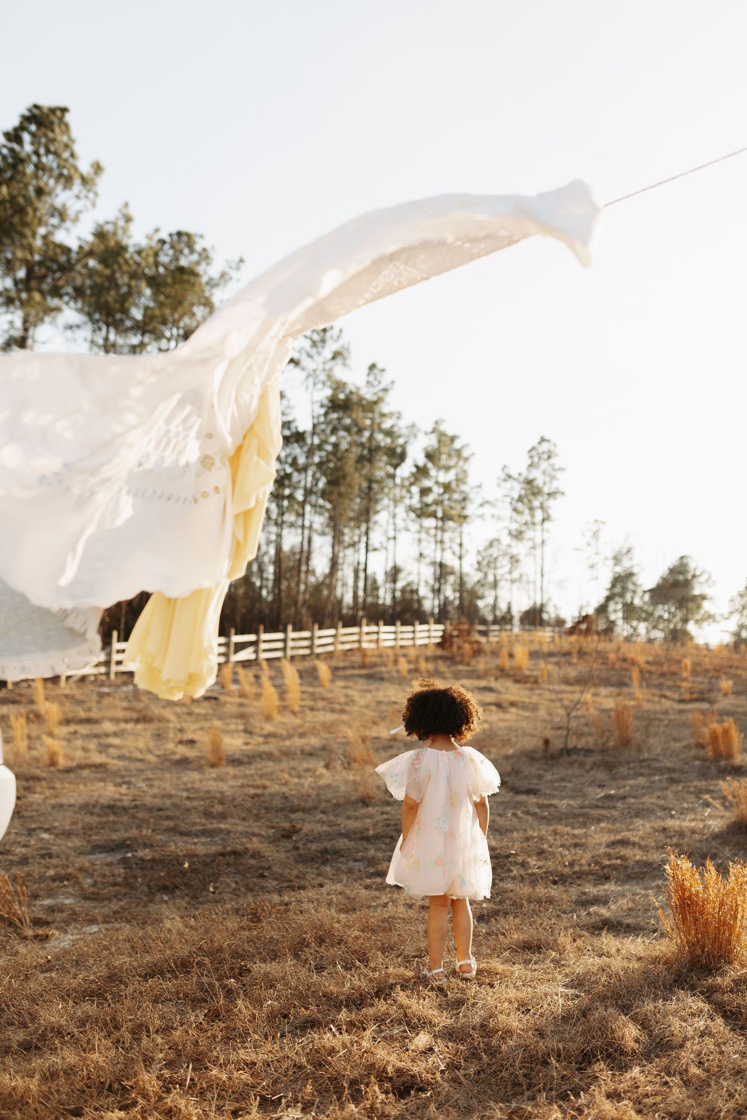 A figure in a white dress runs through a golden field at sunset while holding flowing fabric that billows in the wind.