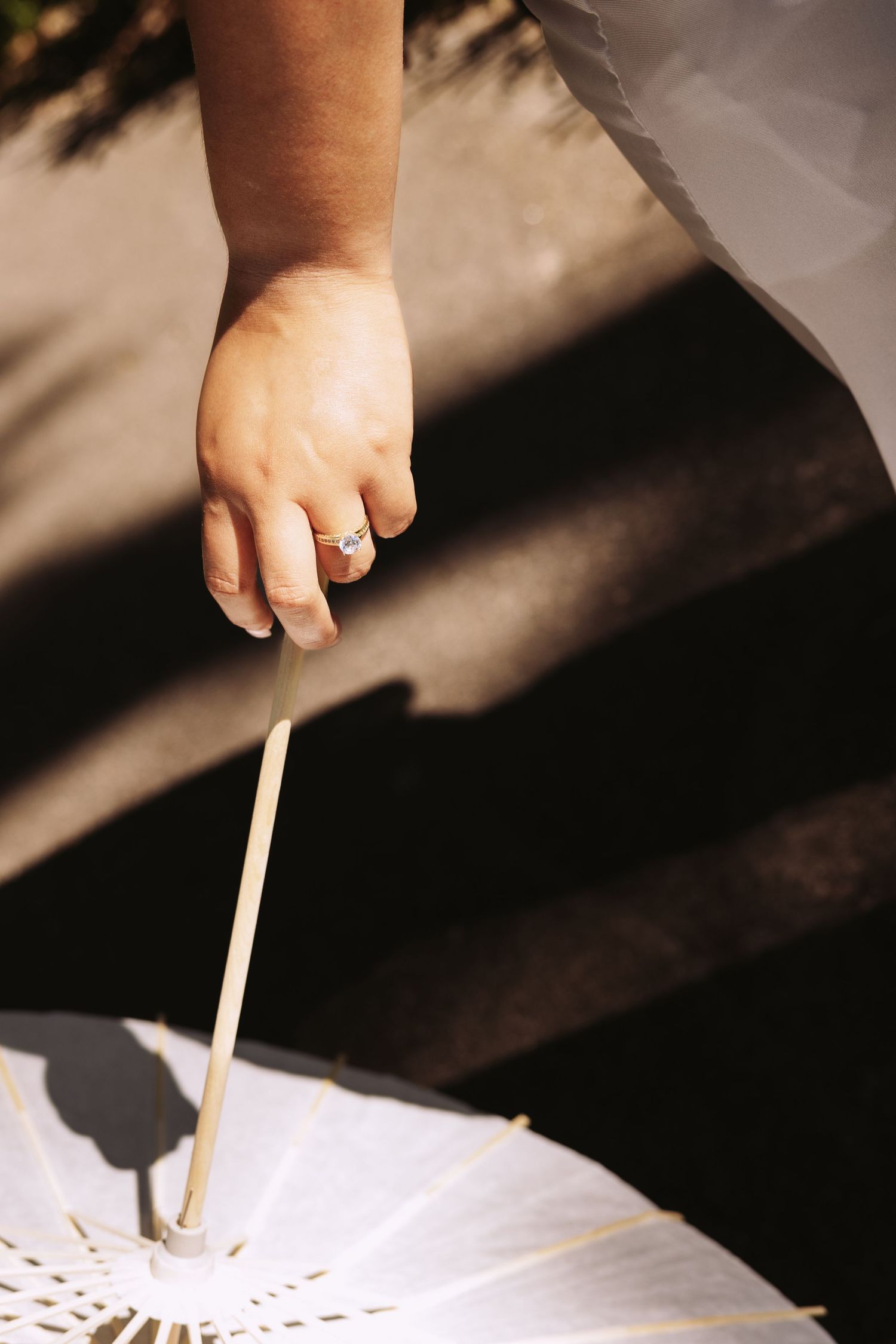 A bride's hand with an engagement ring holding a white parasol umbrella in sunlight.