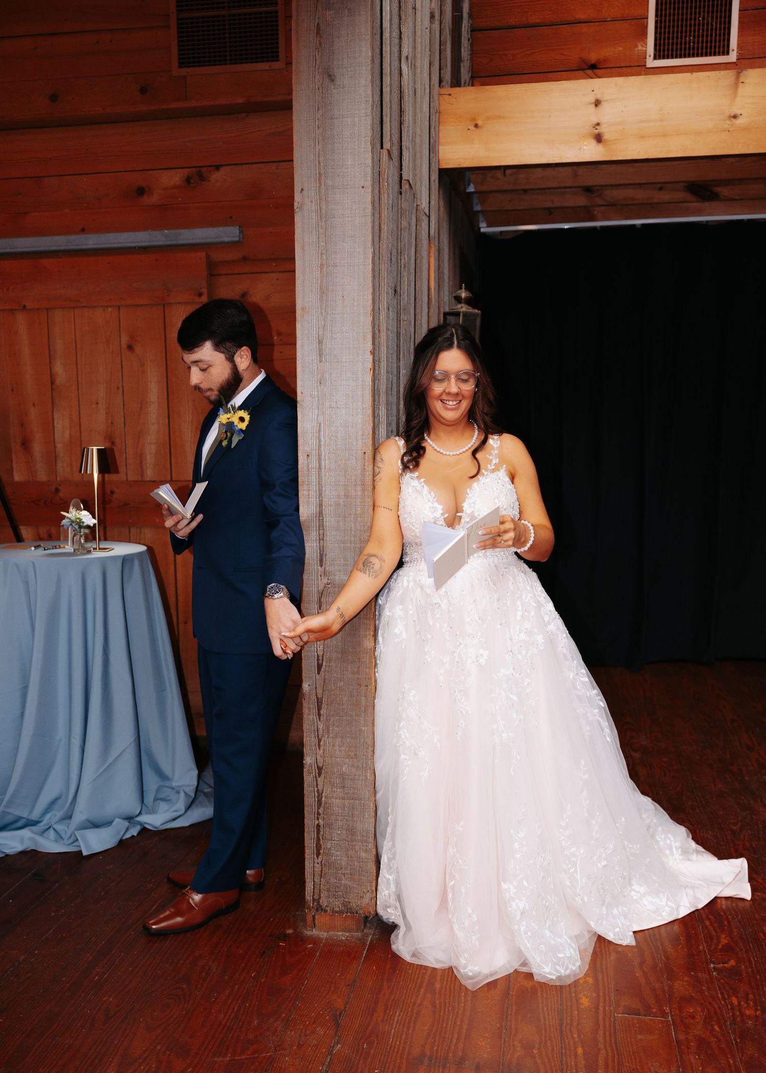Bride and groom exchange vows holding hands around a wooden pillar in a rustic barn wedding venue.