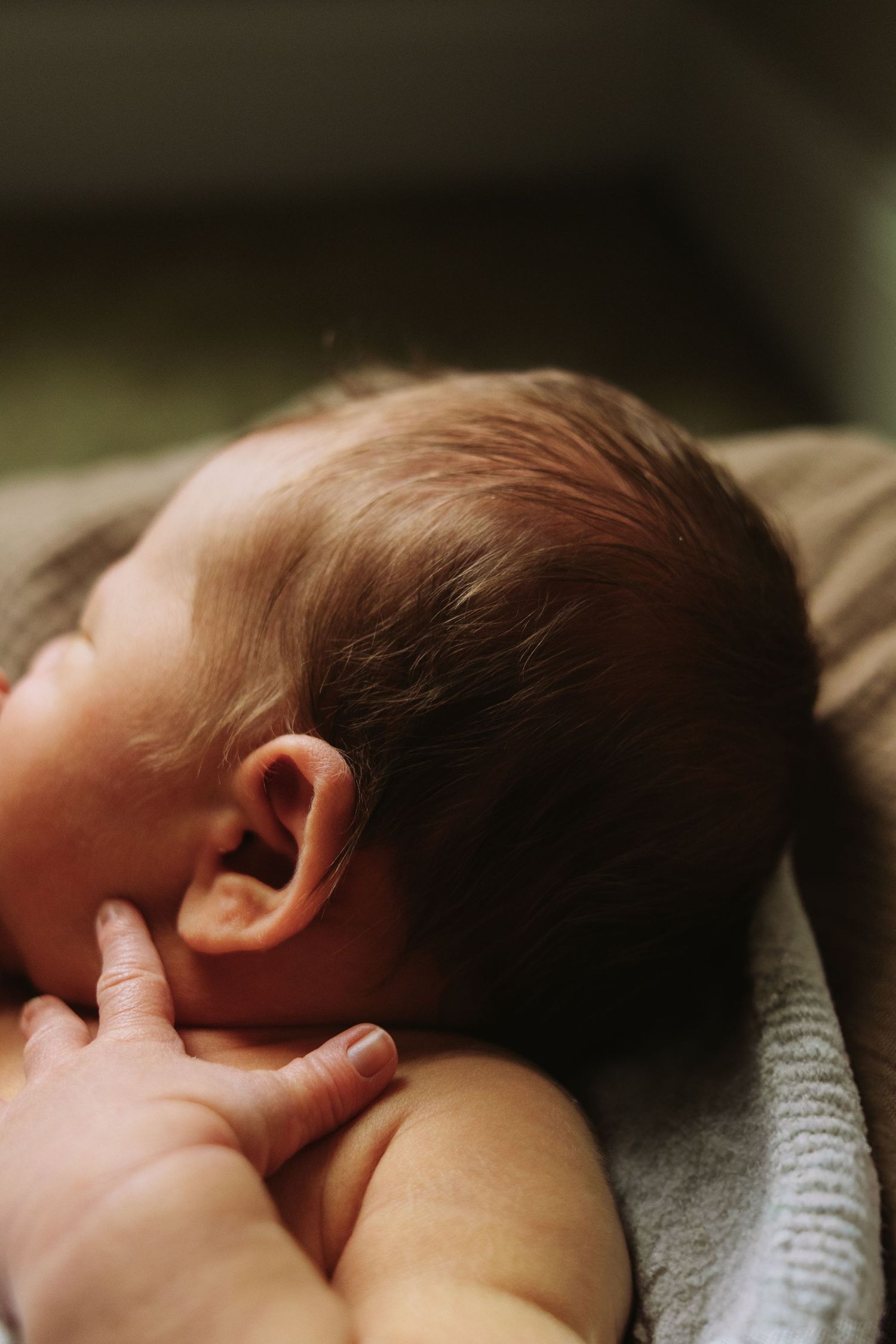 Close-up photo of a sleeping baby's ear and head against soft fabric in warm lighting.
