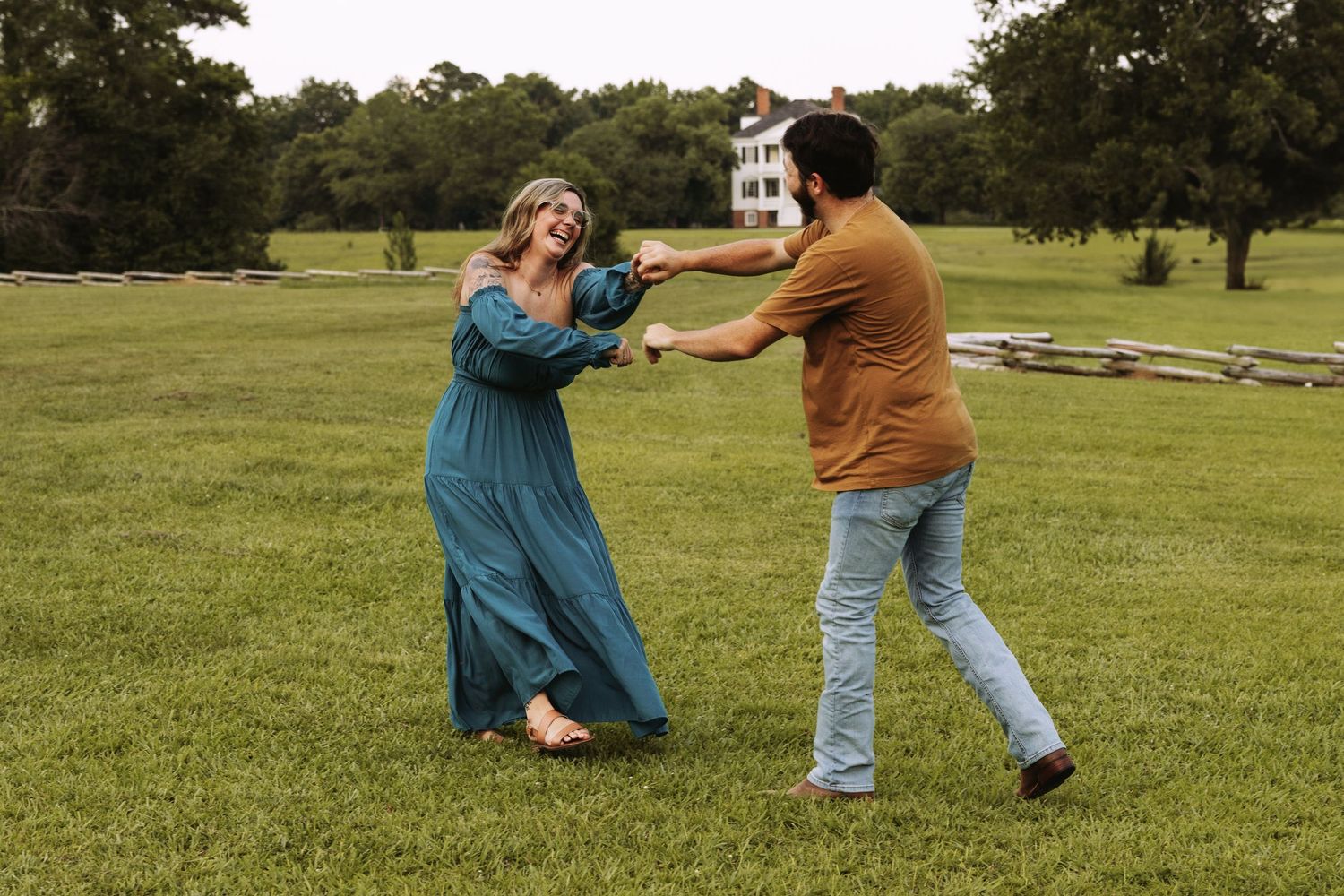 Two people dancing playfully together on a grassy field with trees in the background.