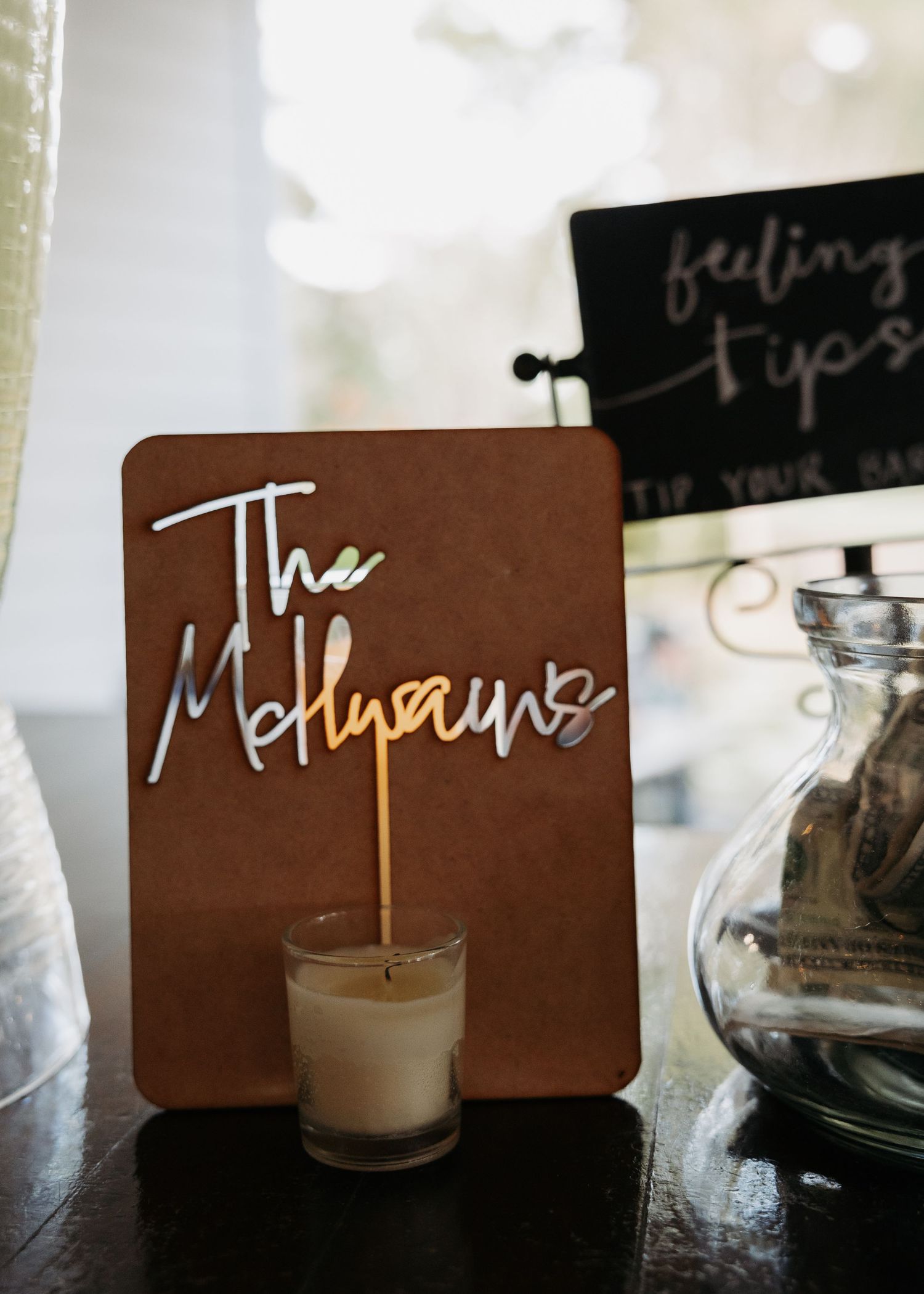 Elegant wedding sign reading The Mellpaeus displayed on a wooden board with a candle at a reception table.