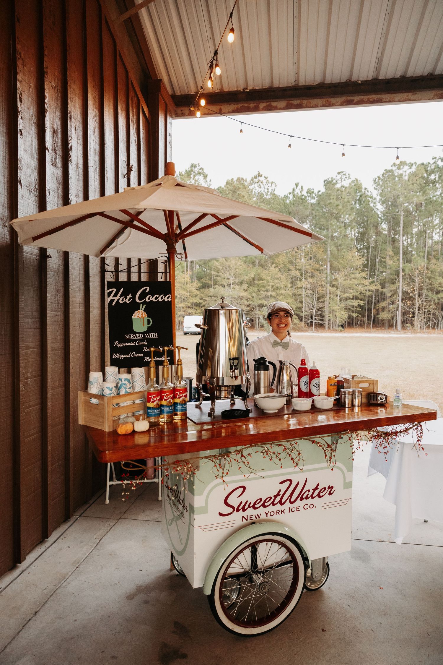 SweetWater New York Ice Co. hot cocoa cart with umbrella at rustic barn wedding venue.