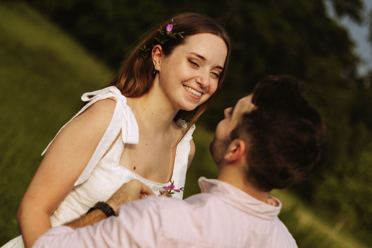 A couple shares a tender romantic moment while sitting together outdoors in a sunny natural setting.