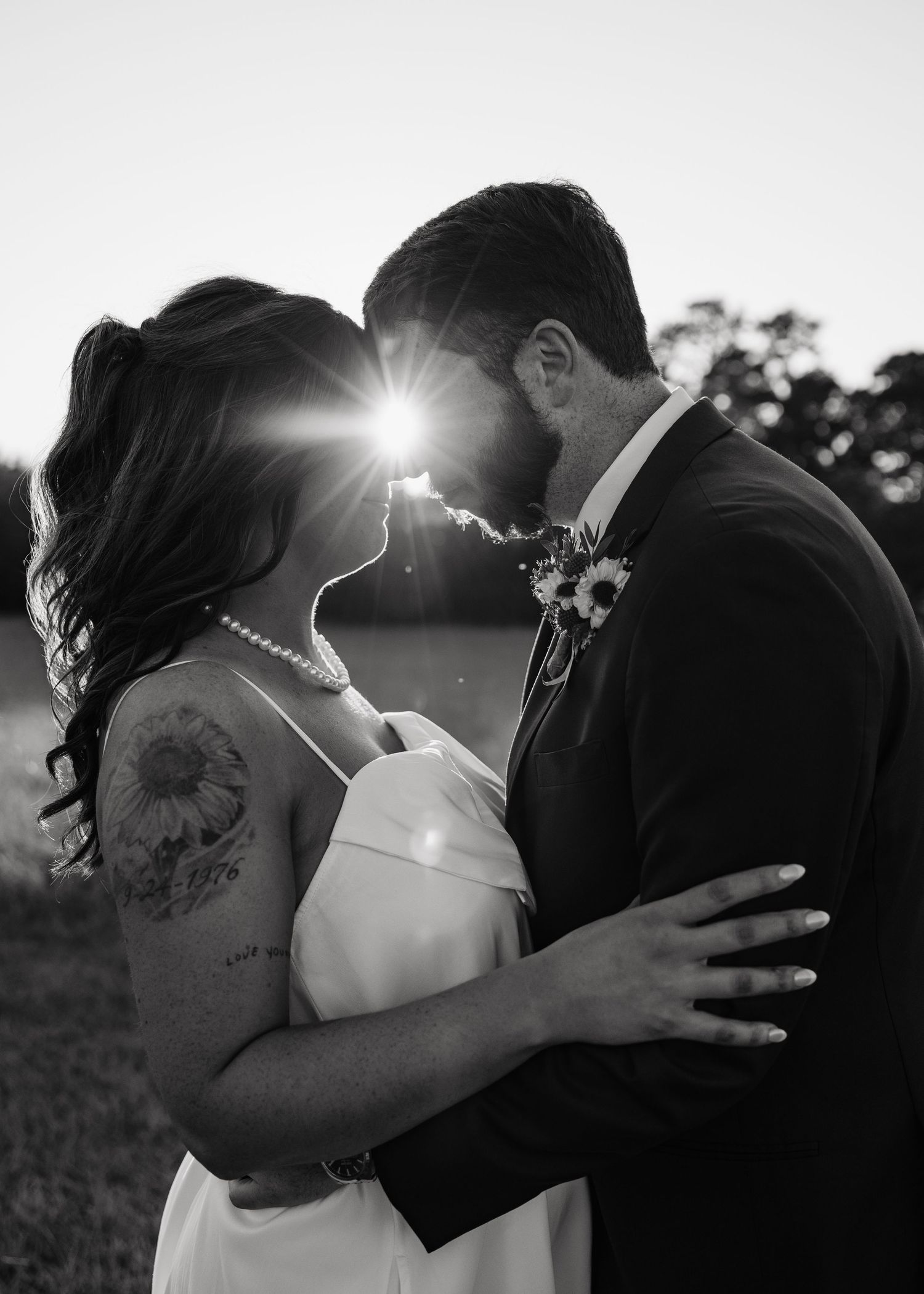 Black and white sunset portrait of bride and groom embracing with sunflare between them.