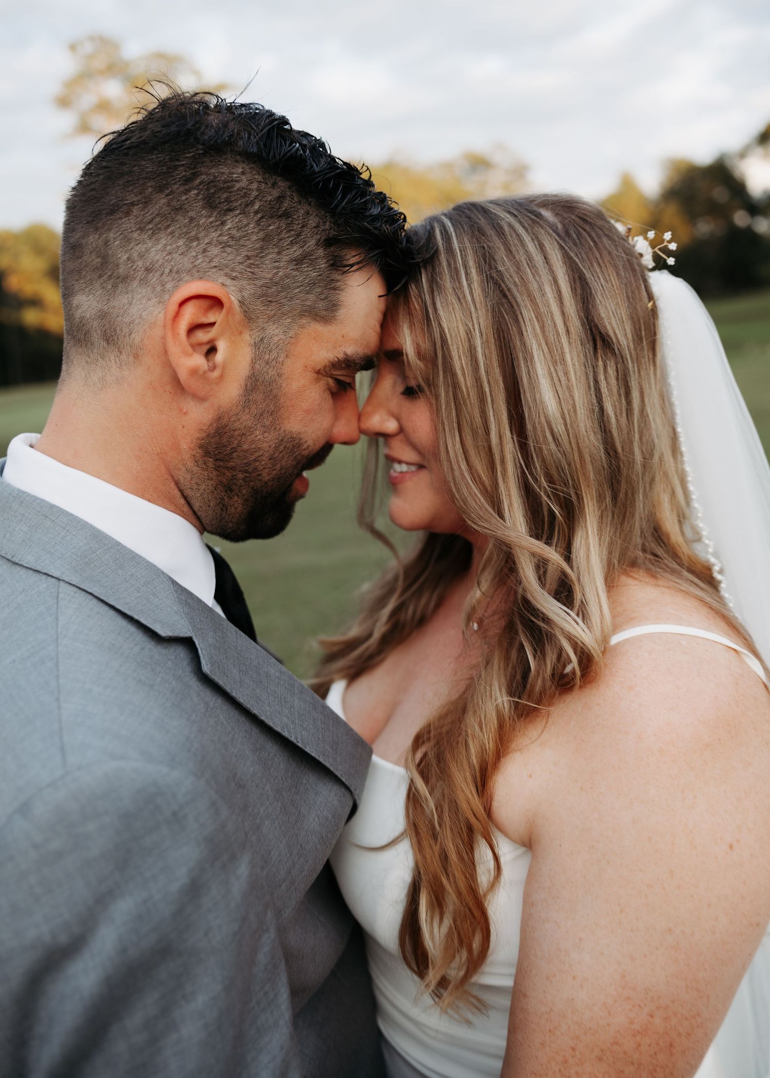 Bride and groom touching foreheads romantically outdoors on their wedding day at golden hour.