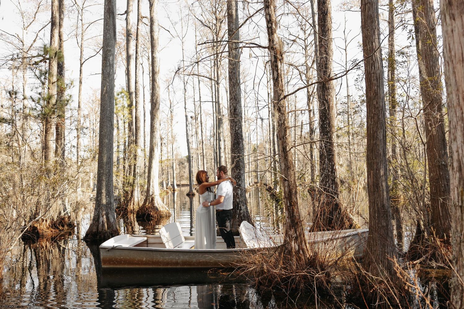 Couple sharing a romantic moment on a wooden boat surrounded by cypress trees in a serene swamp setting.