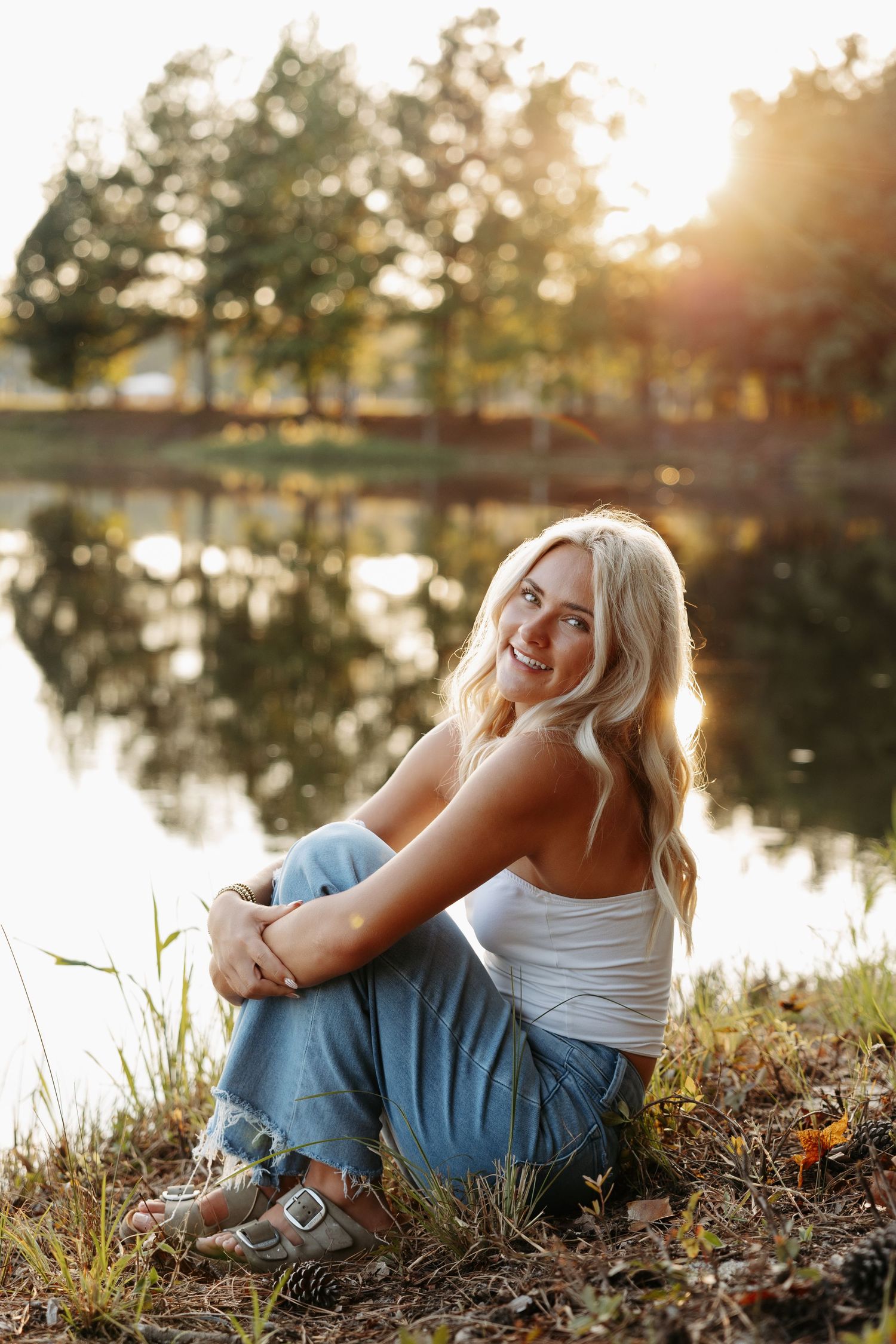 A couple sits together by a tranquil lake during golden hour sunset, creating a peaceful nature moment.