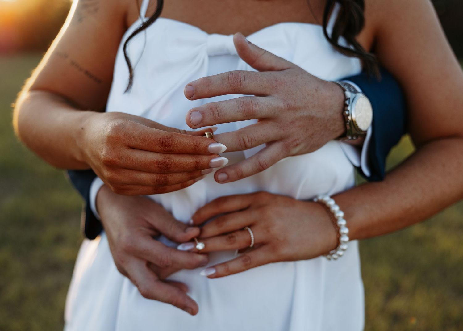 Close-up of couple holding hands showing wedding rings at golden hour.
