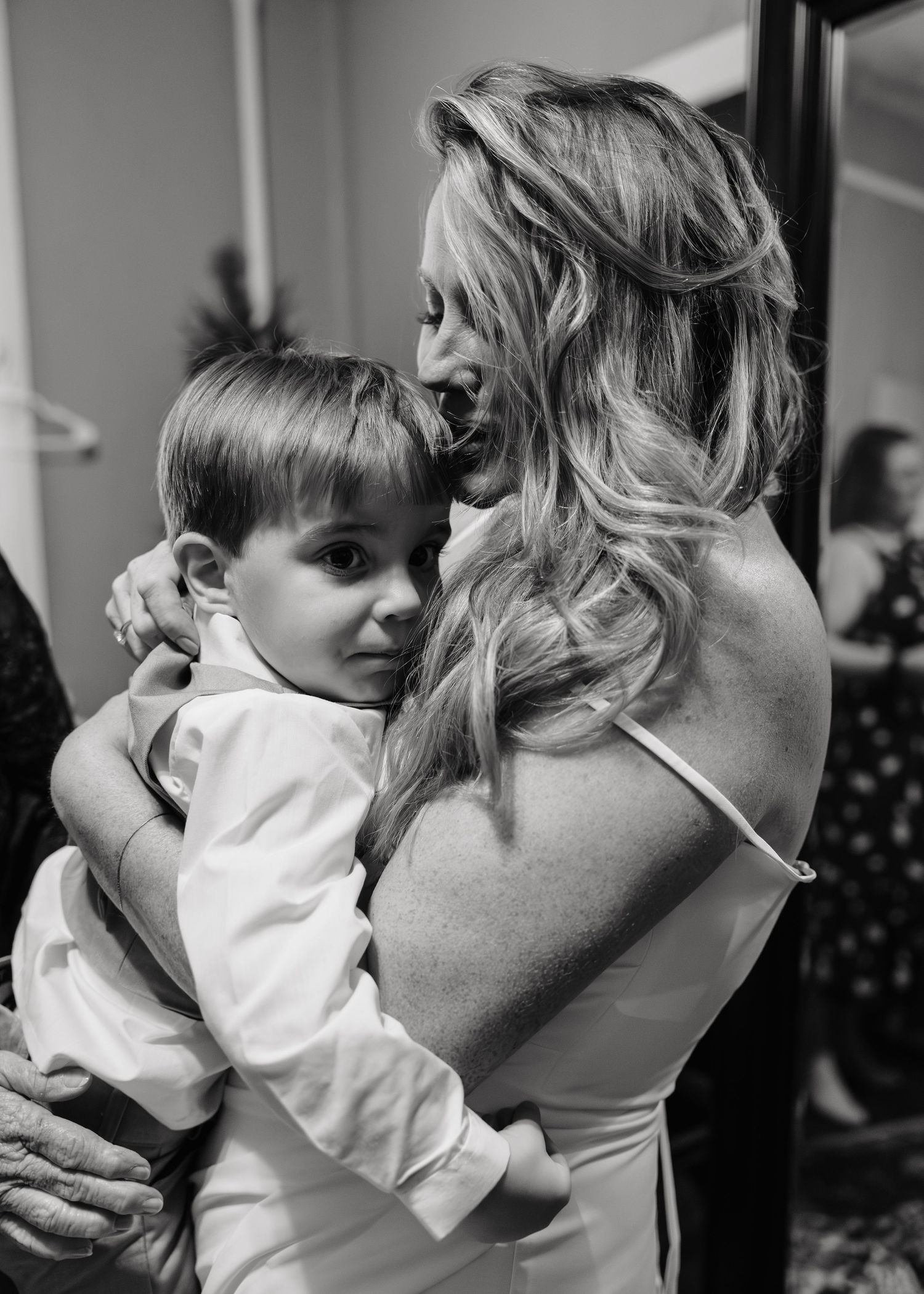 Black and white photo of a blonde woman in a wedding dress tenderly holding a young boy in a white dress shirt.