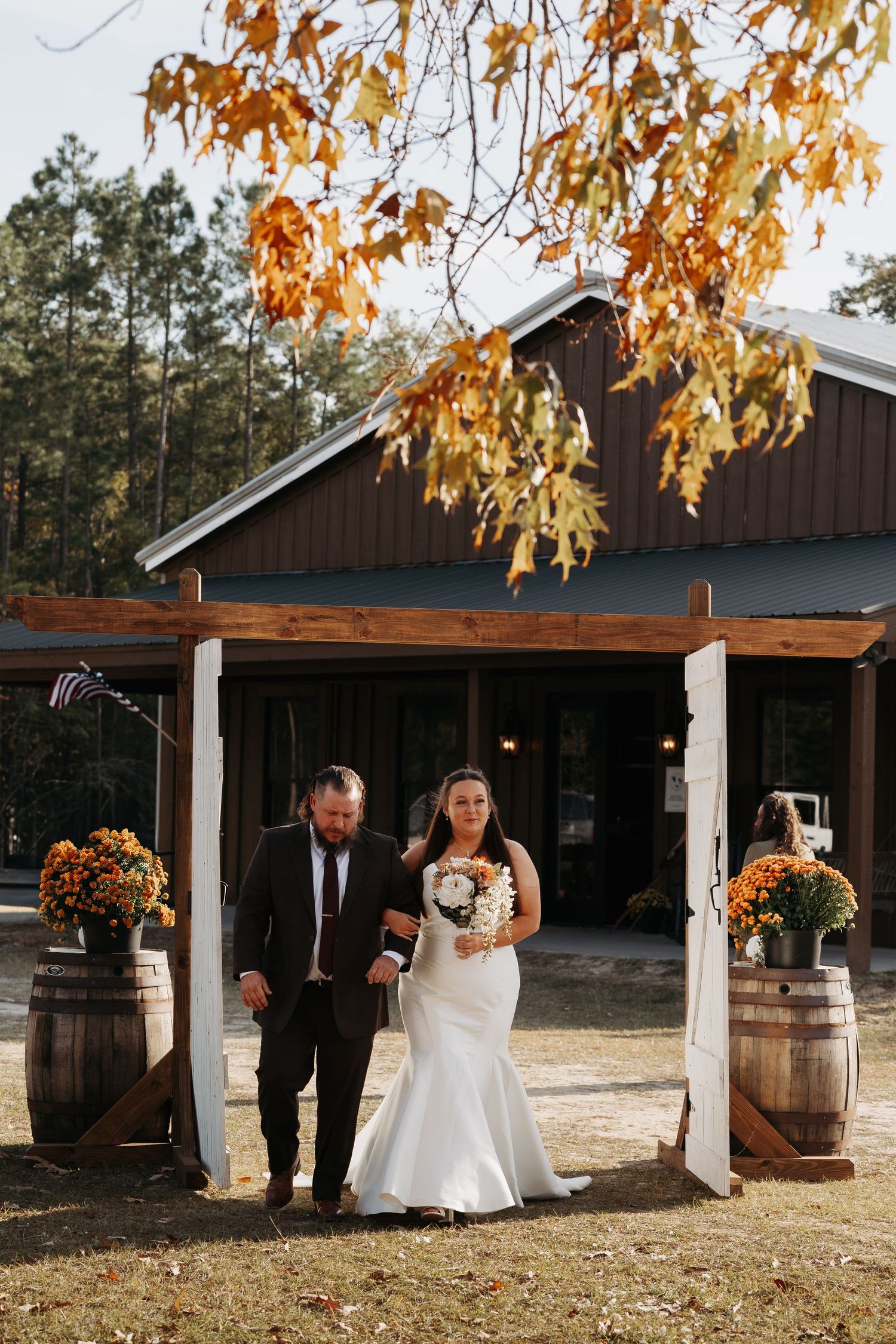 Bride and groom exiting fall wedding ceremony through wooden arch with orange floral decor.