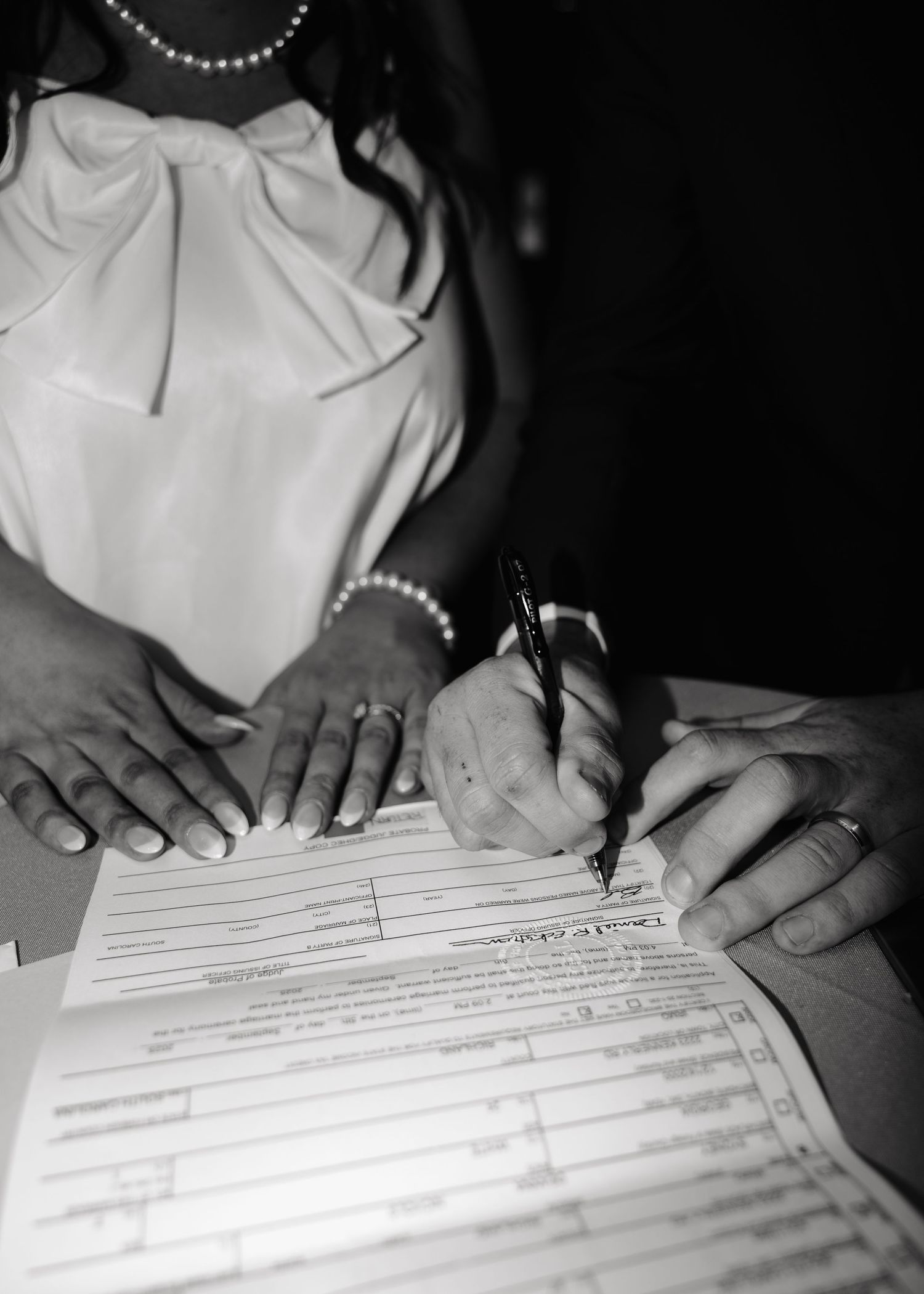 Bride in white dress signing wedding certificate with pen at reception table.