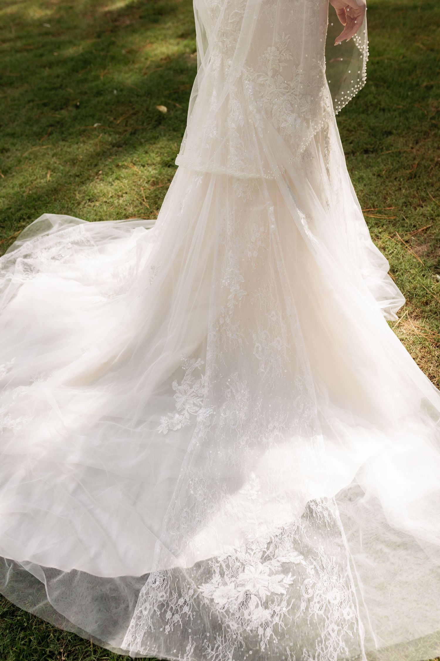 Elegant white lace wedding gown with a long flowing train displayed outdoors on green grass.