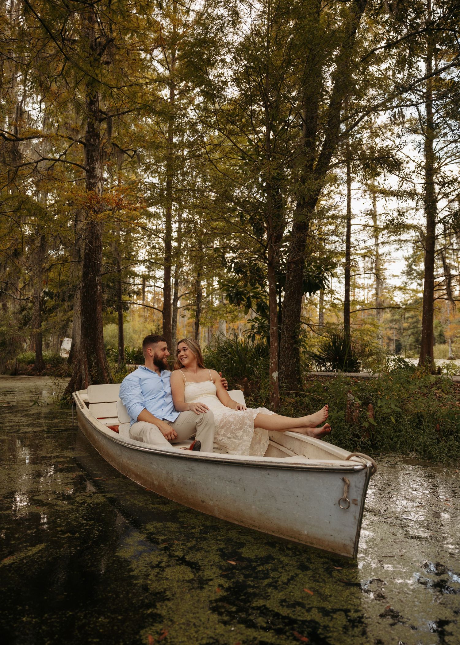 A couple lounges together in a romantic outdoor setting with a canoe and autumn foliage in the background.