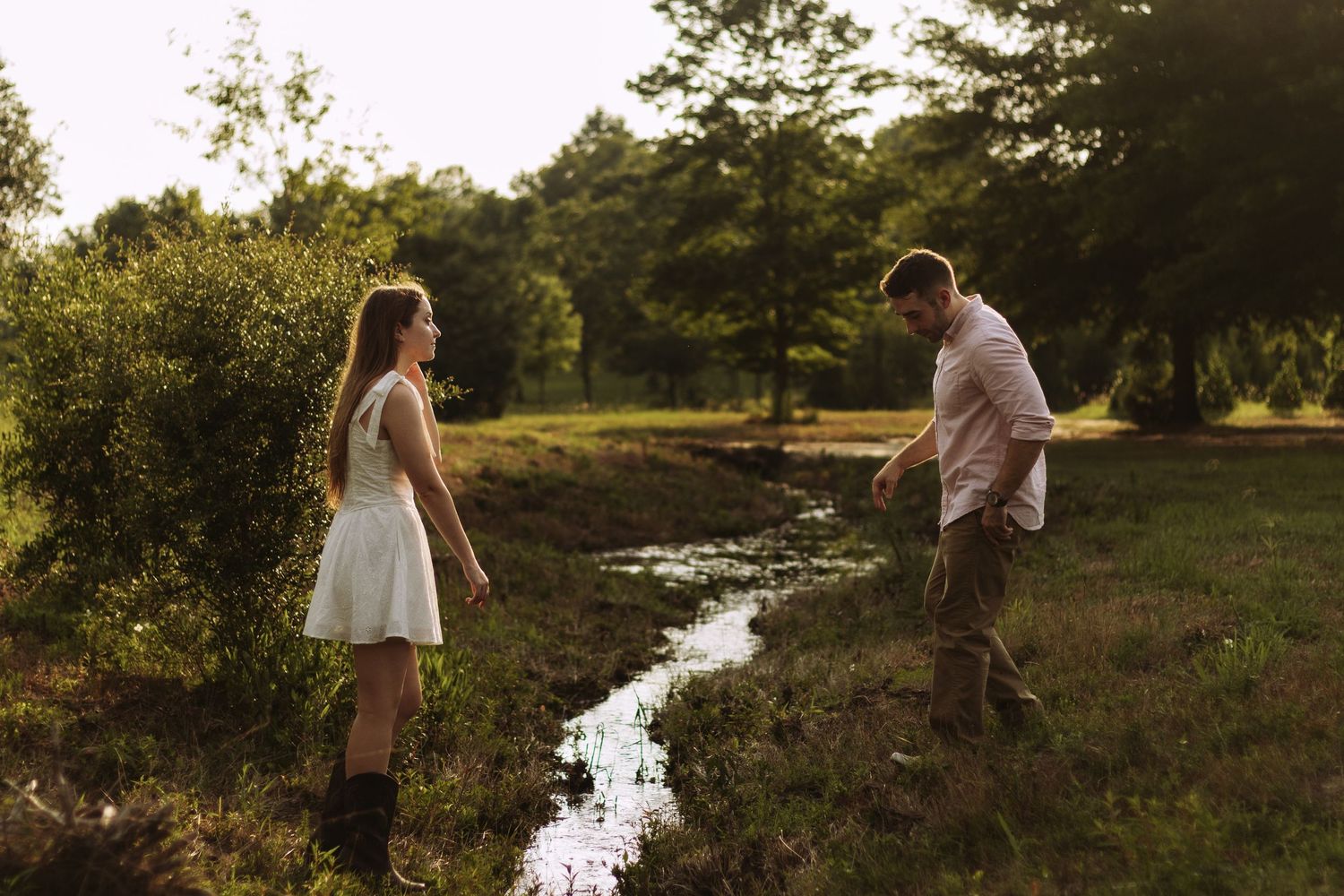 Romantic couple strolls along winding creek at golden sunset in rural countryside.