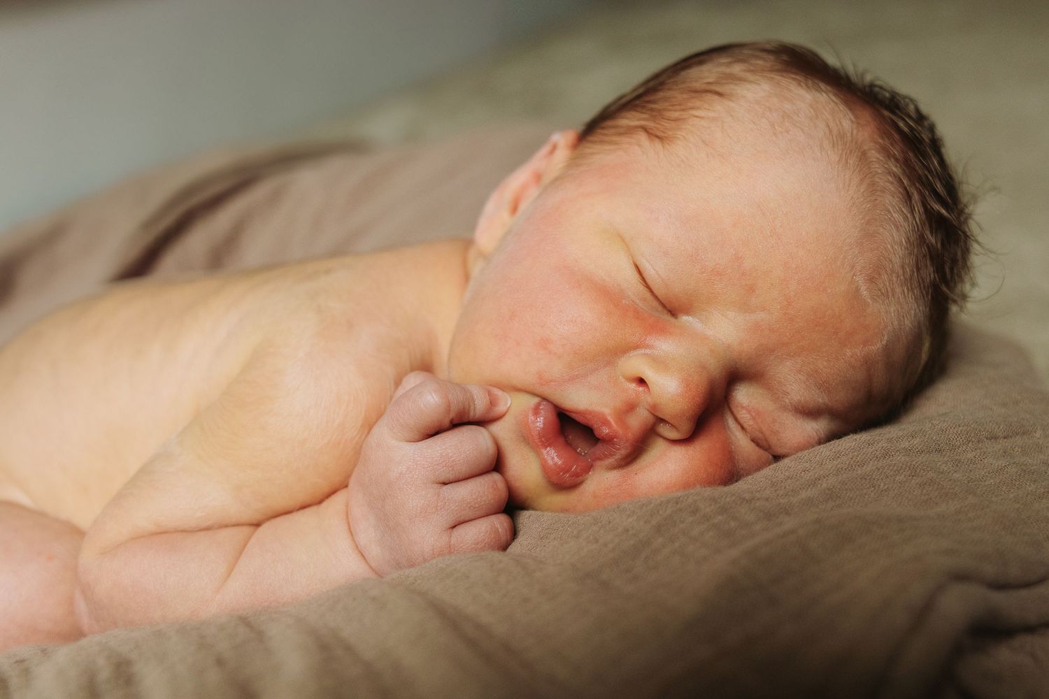 A sleeping newborn baby lies peacefully on soft beige fabric in a tender and serene pose.