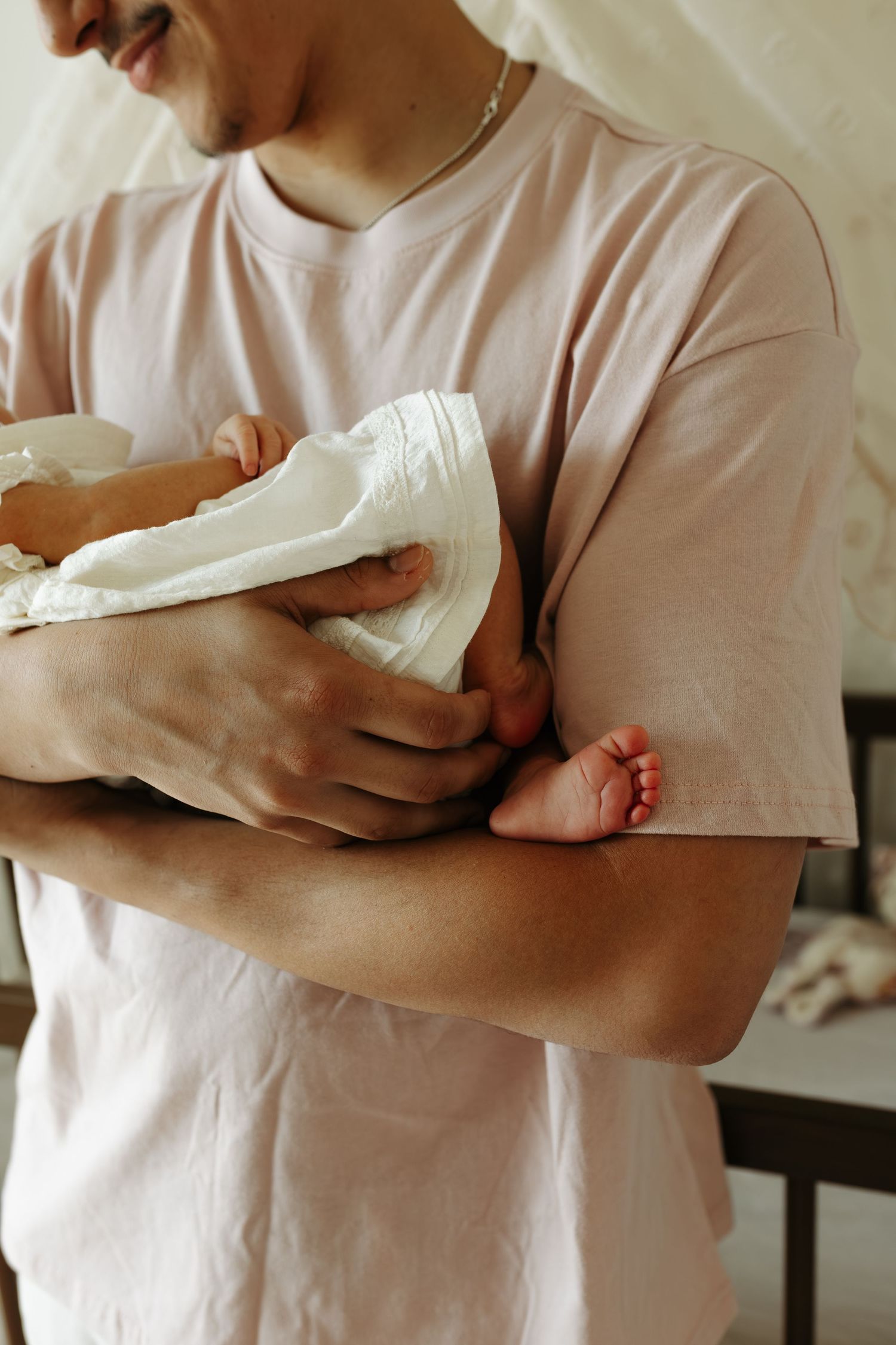 A parent in a pink t-shirt tenderly holds a swaddled newborn baby, with tiny feet visible.
