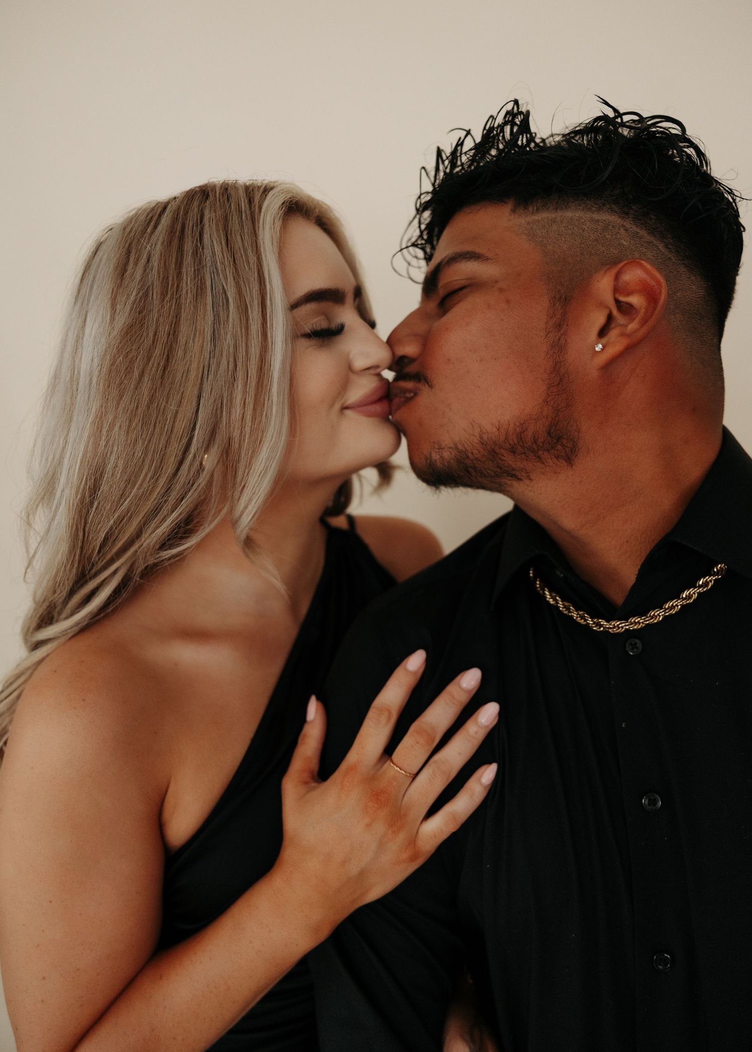 Couple in black outfits sharing a romantic kiss, woman with blonde hair placing hand on mans chest.