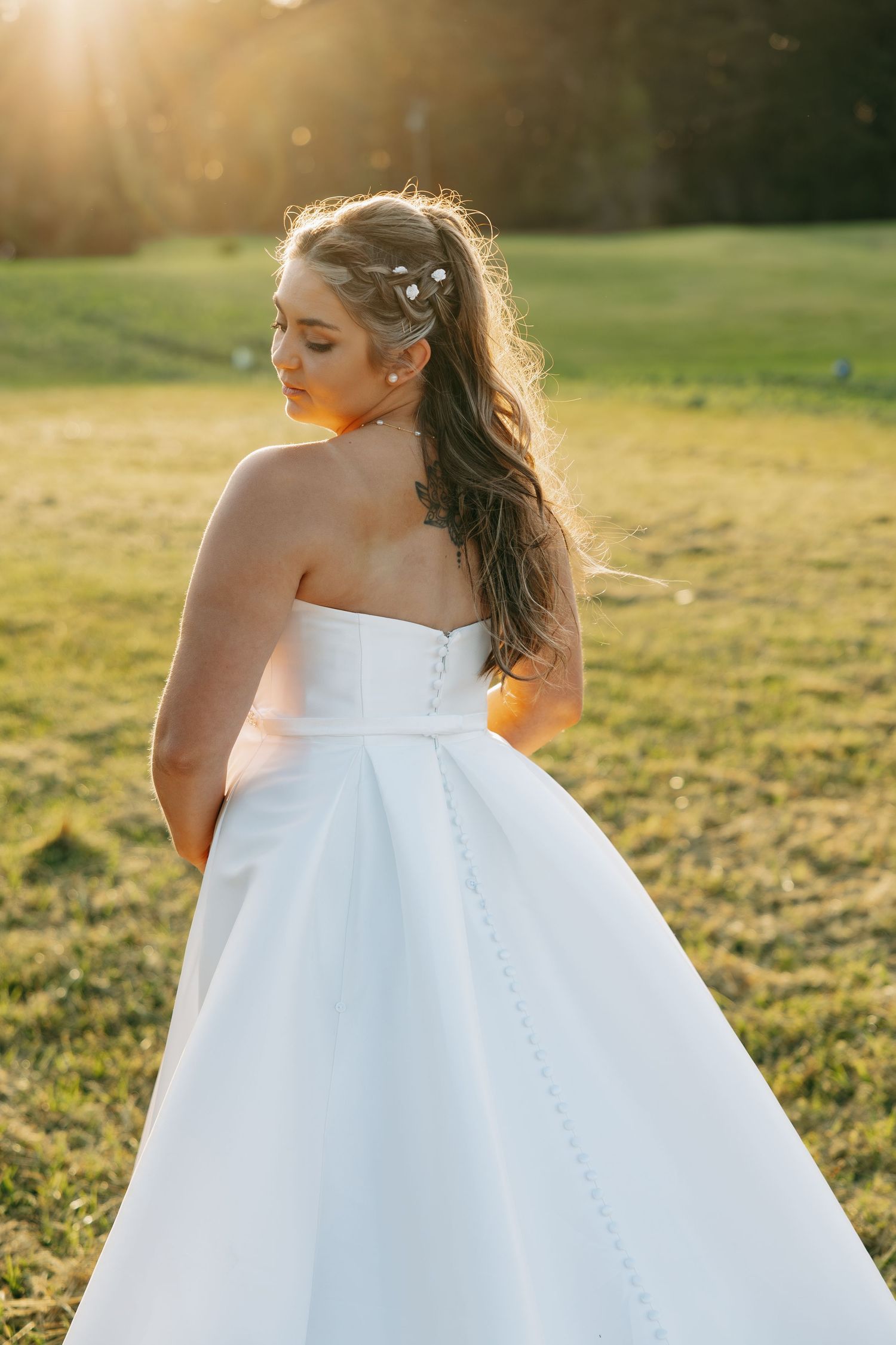 Bride in a strapless white ball gown with floral hair accessories poses in a sunlit green field.