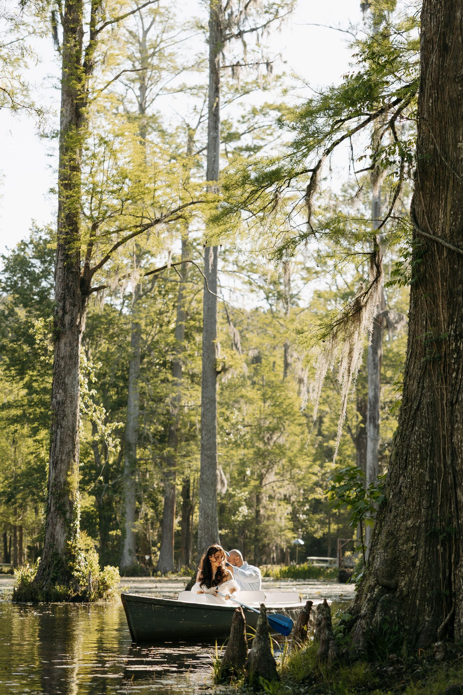 Couple sitting in a rowboat surrounded by tall cypress trees draped in Spanish moss on a serene lake.